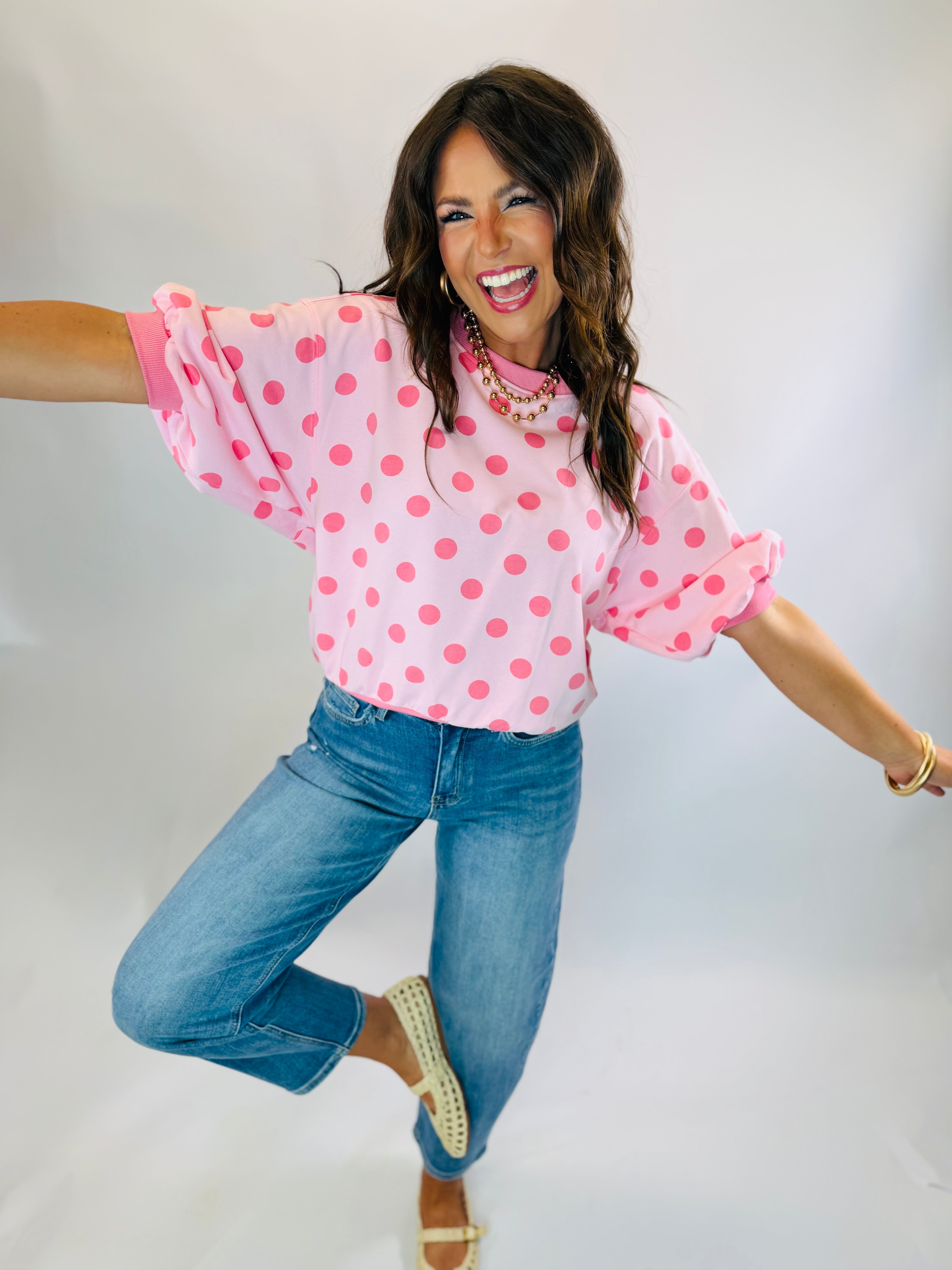 Woman wearing Parker Top in light pink with hot pink polka dots, paired with blue jeans.