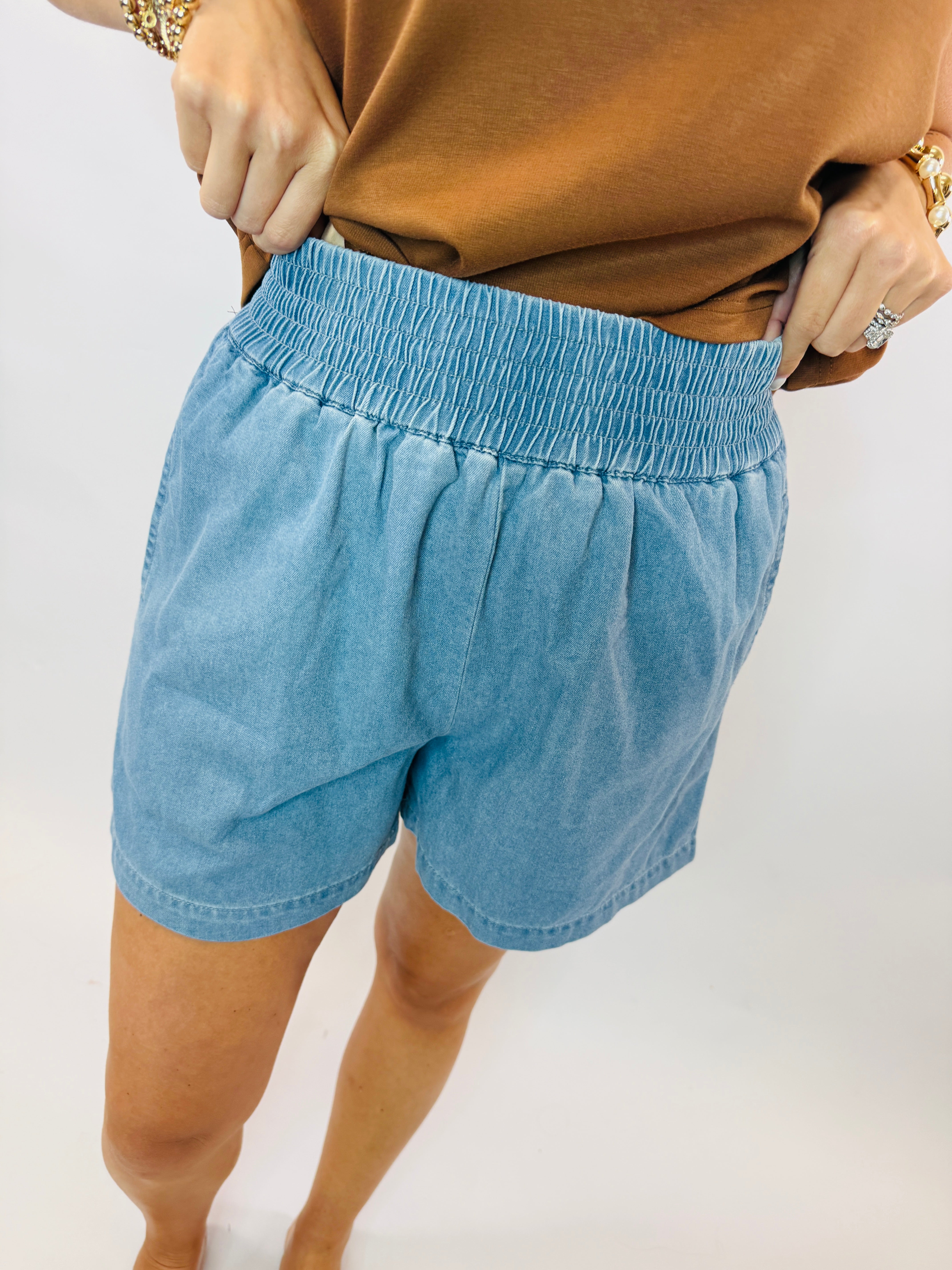 Light blue denim pull-on shorts with elastic waistband worn with camel colored top