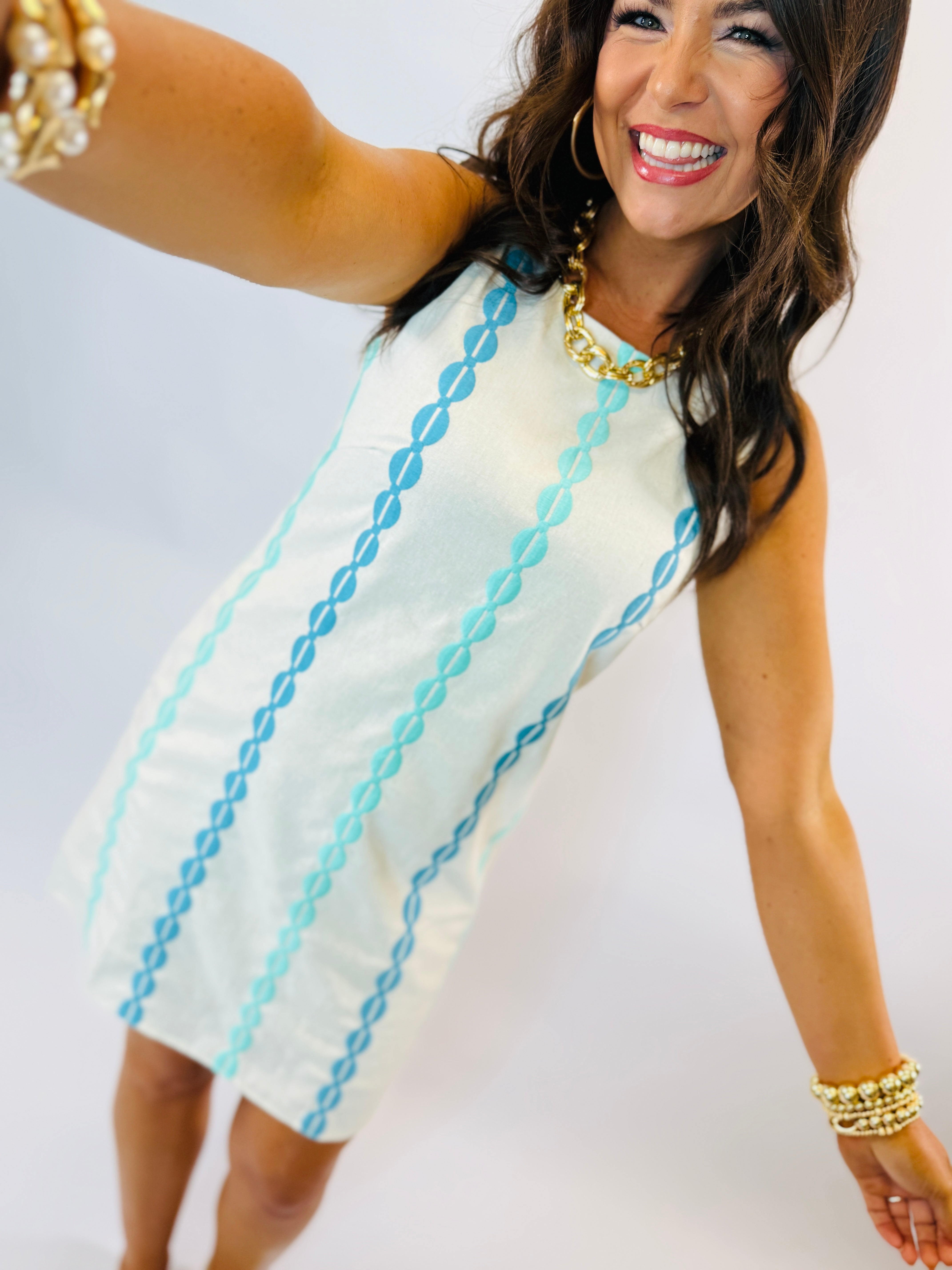 Woman wearing white sleeveless dress with blue chain print pattern and gold jewelry accessories