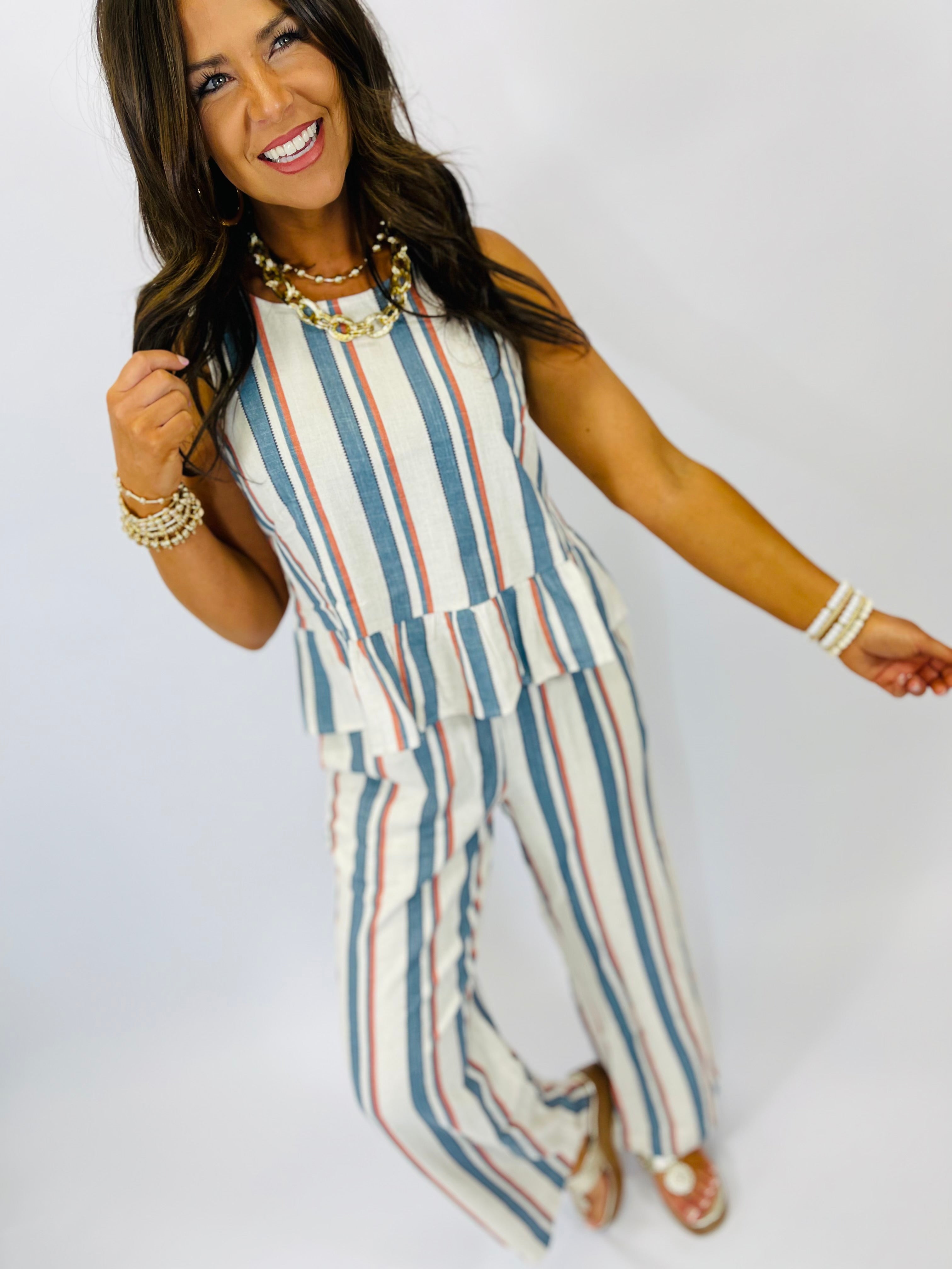 Woman wearing striped sleeveless top with blue, coral and white vertical stripes, styled with statement jewelry.