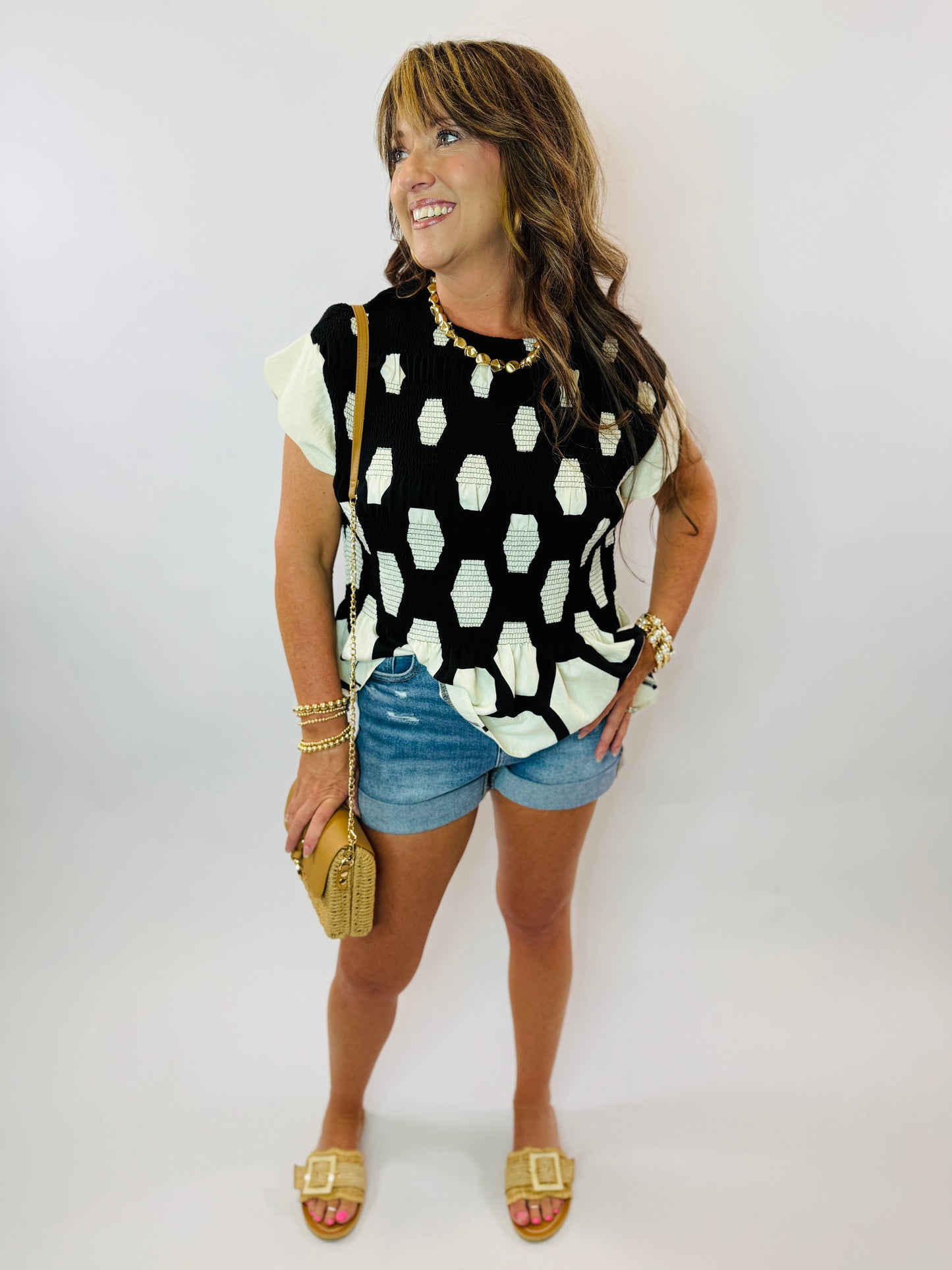 Woman wearing black and white hexagonal patterned Caroline top with white cap sleeves, paired with denim shorts and gold a...