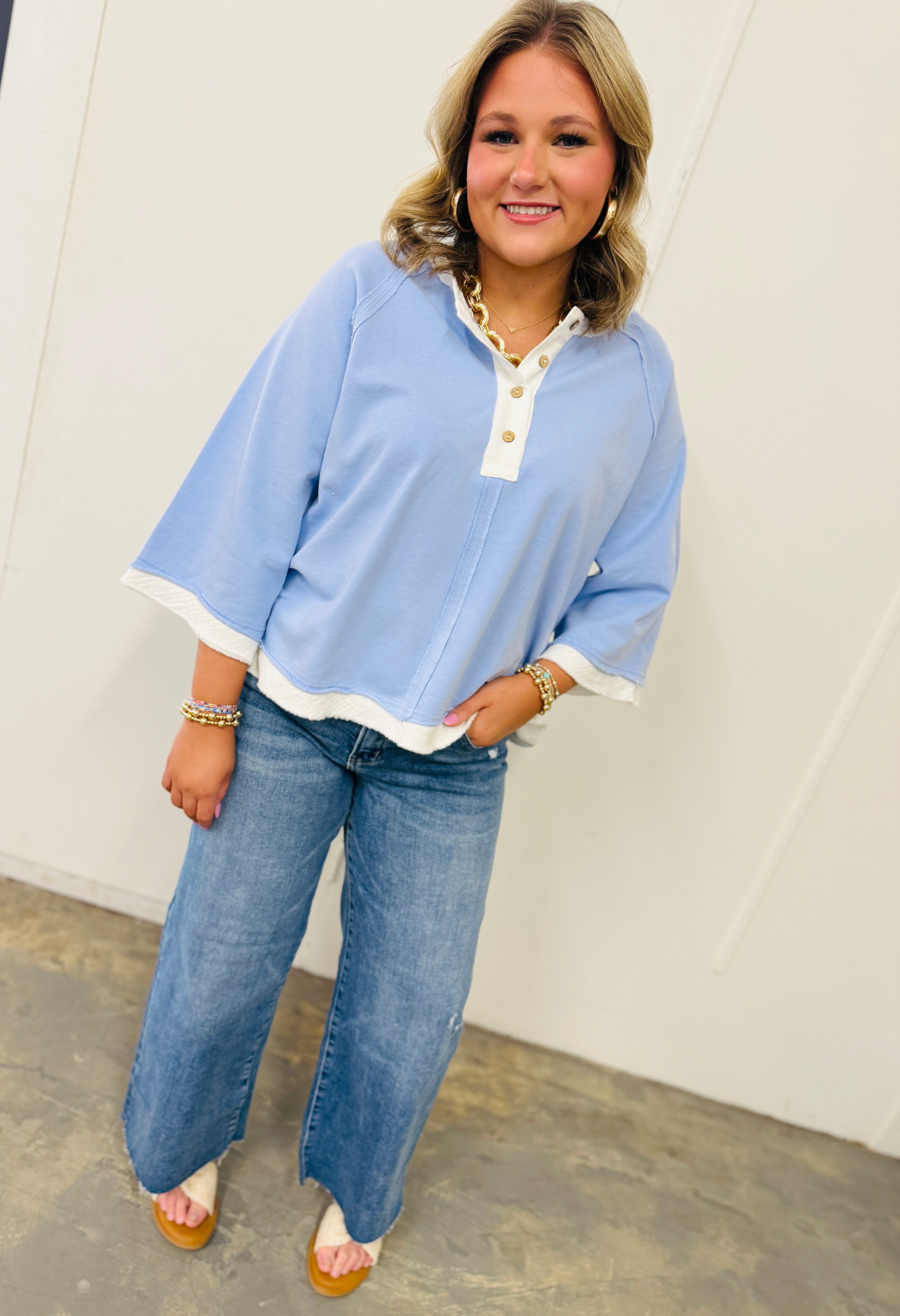 Woman wearing light blue Elizabeth top with white contrast trim and gold buttons, paired with wide-leg jeans.