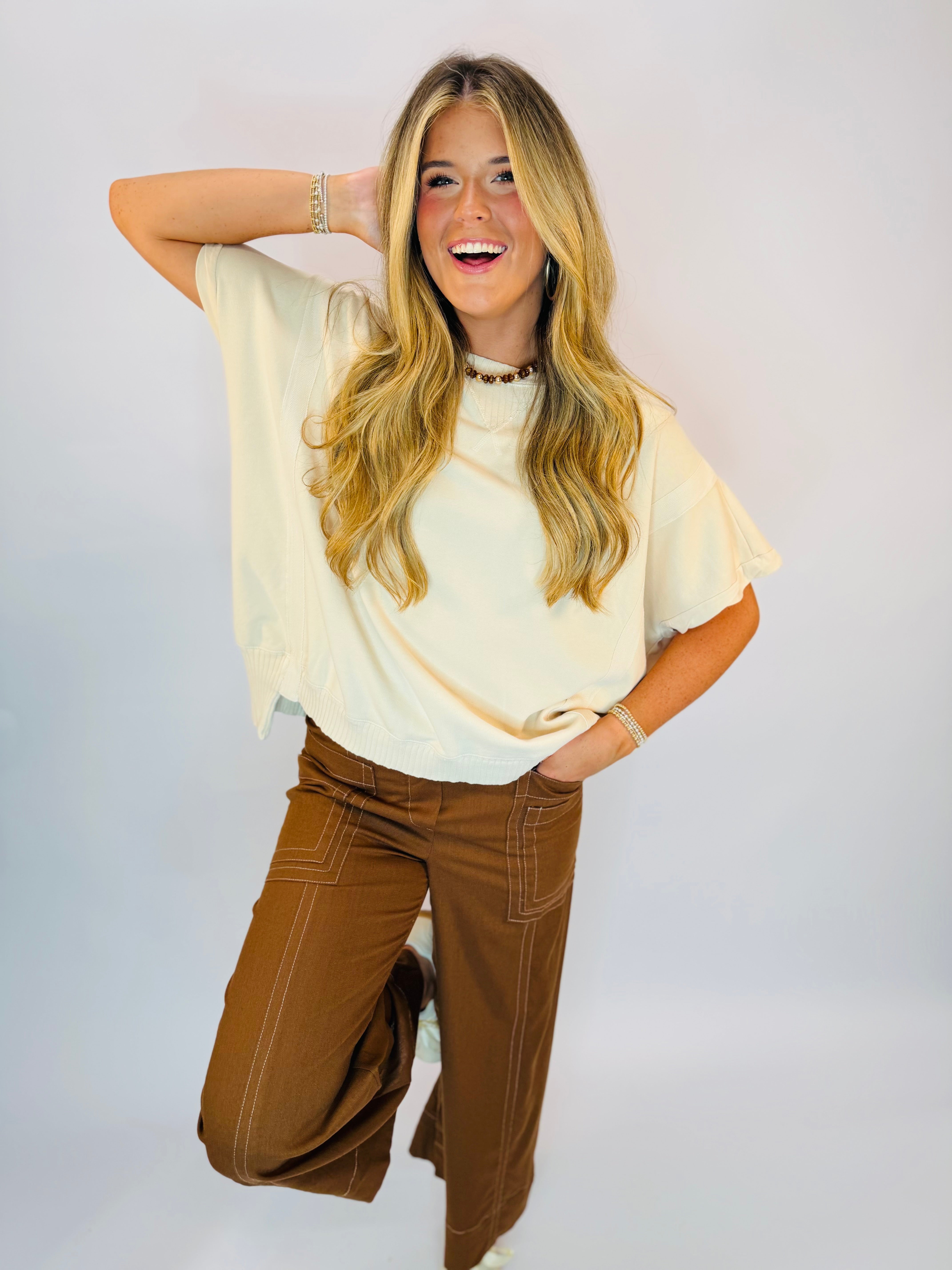 Cream short-sleeve flutter top with relaxed fit, paired with brown wide-leg pants.