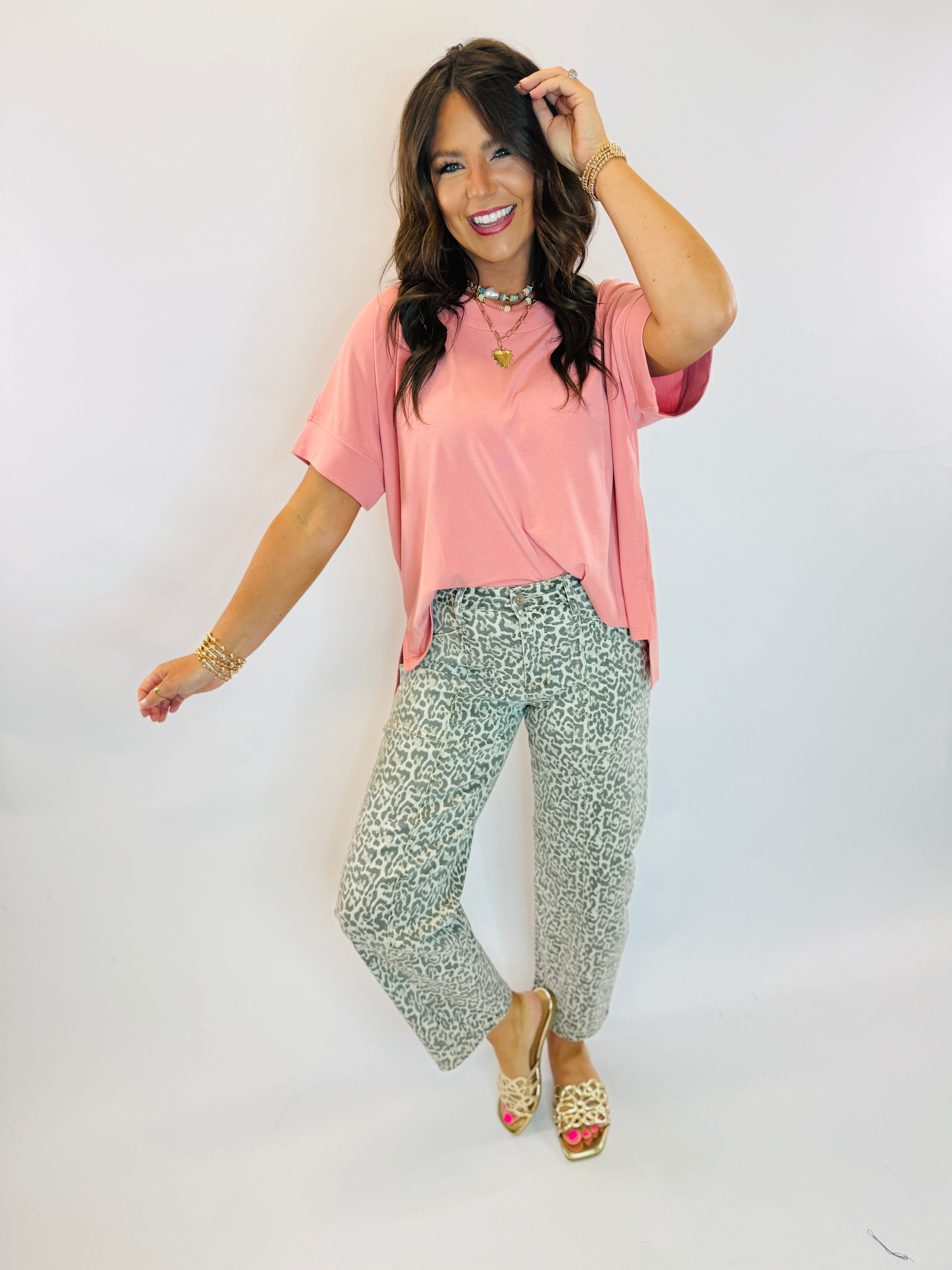 Woman wearing sage green leopard print barrel-leg denim jeans paired with a pink top and gold sandals.