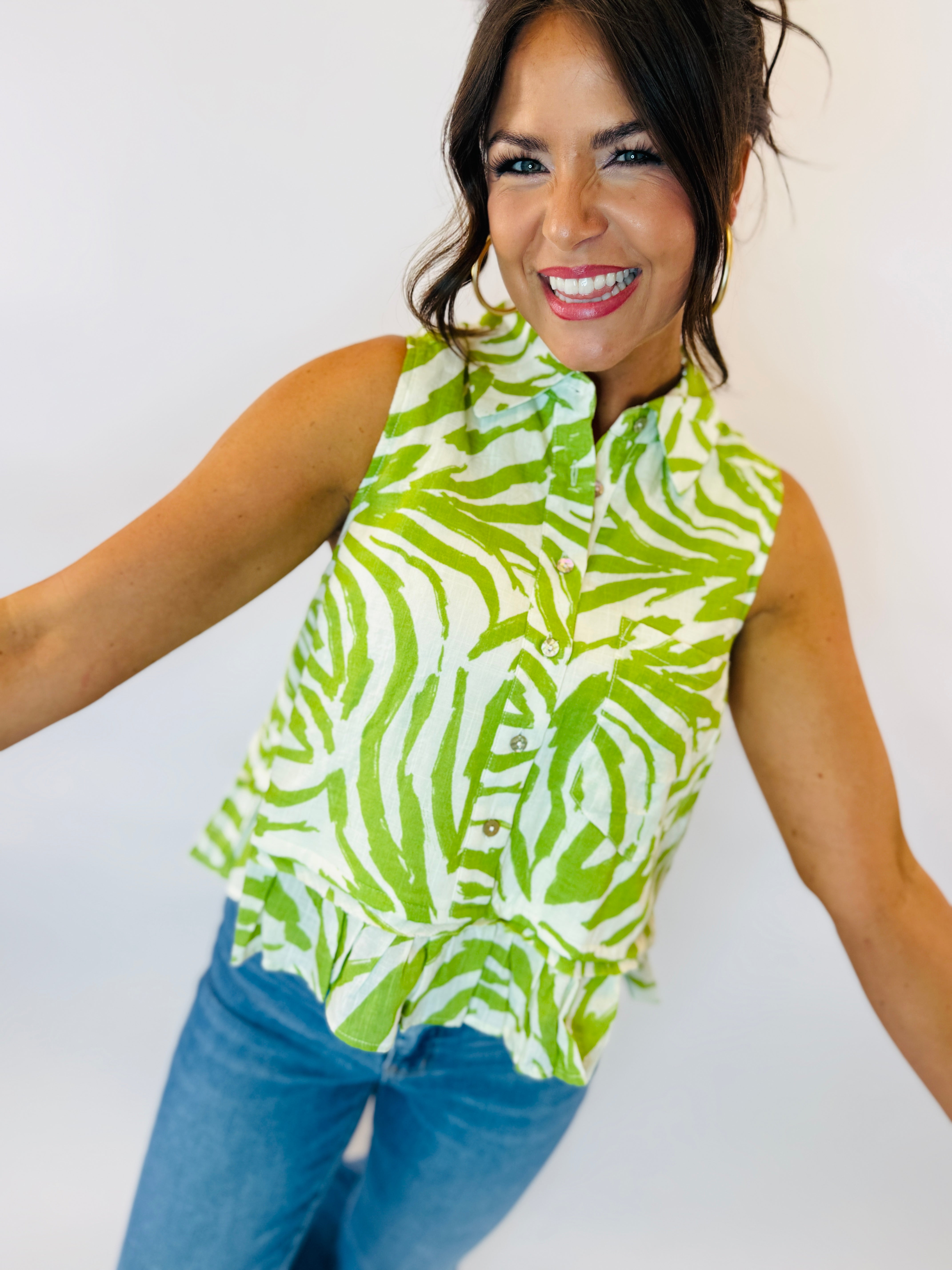 Woman wearing green and white zebra print sleeveless button-up top with blue jeans, smiling at camera.