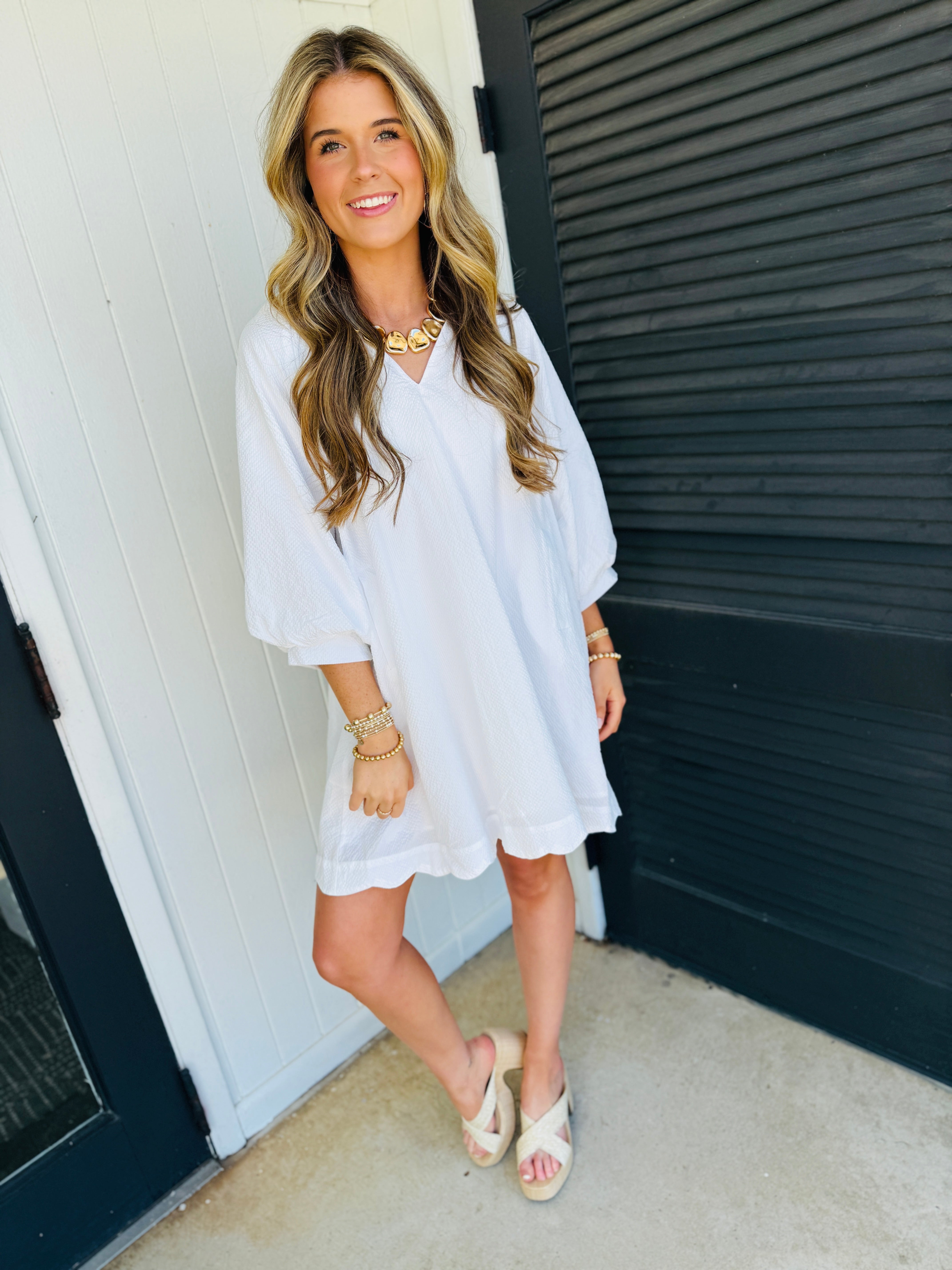 Woman wearing white long-sleeve Libby Maple Classic Dress with gold jewelry and nude wedge sandals