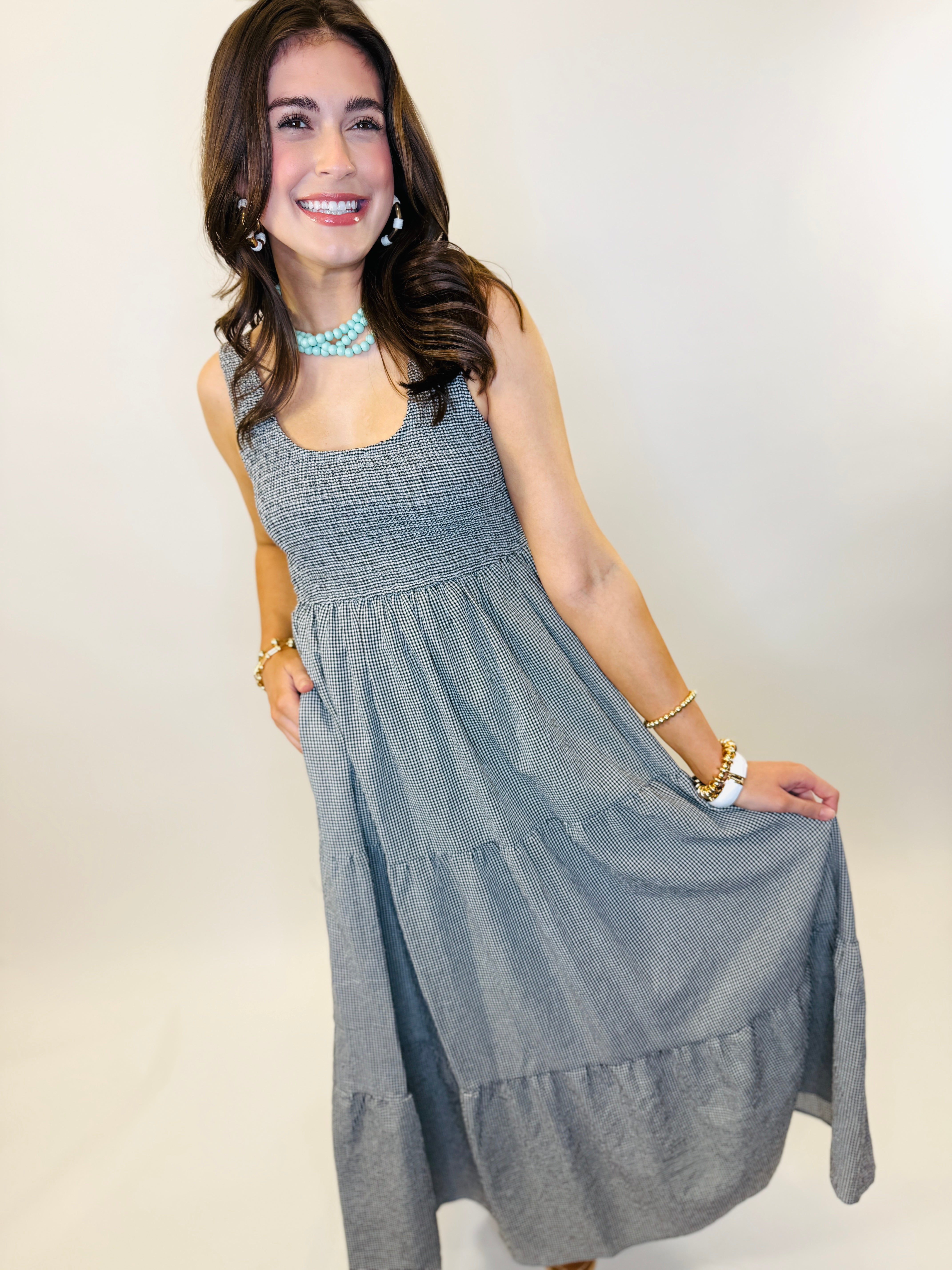 Woman wearing gray gingham sleeveless midi dress with smocked bodice and tiered skirt, styled with turquoise jewelry.