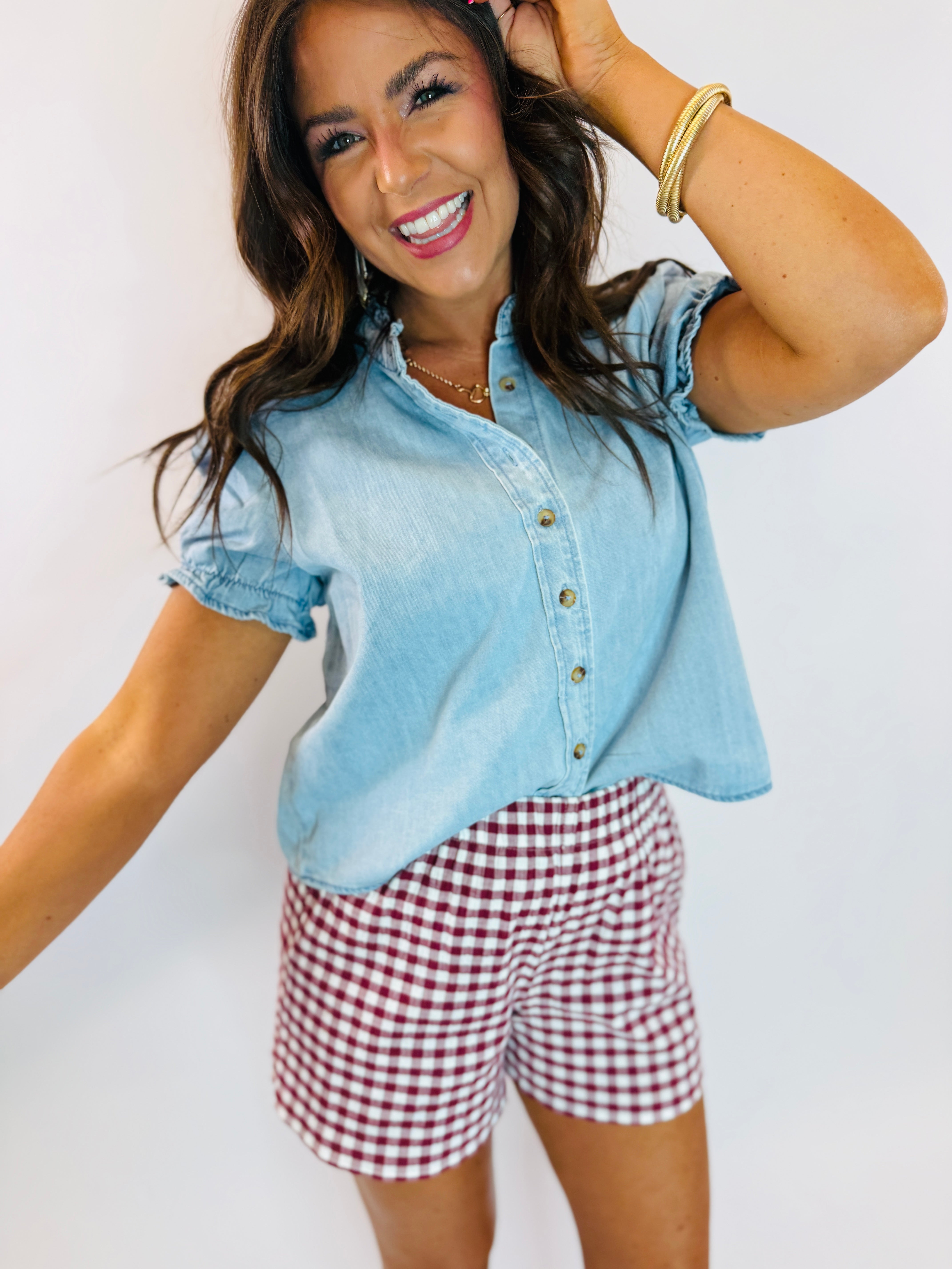 Light blue chambray button-up top with ruffle sleeves and scalloped hem, styled with gingham shorts.