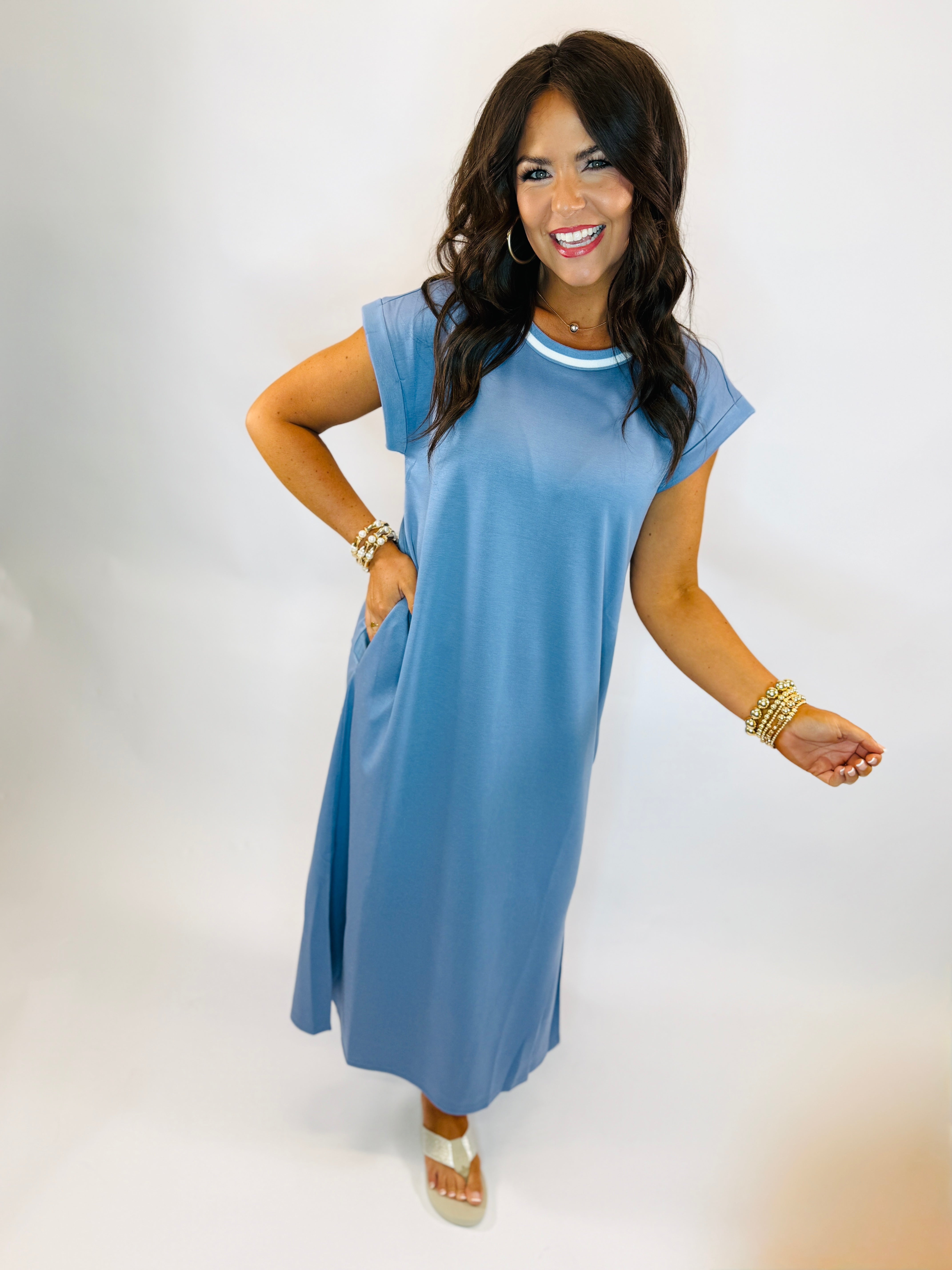 Woman wearing blue casual midi dress with short sleeves and white trim neckline, styled with gold jewelry.