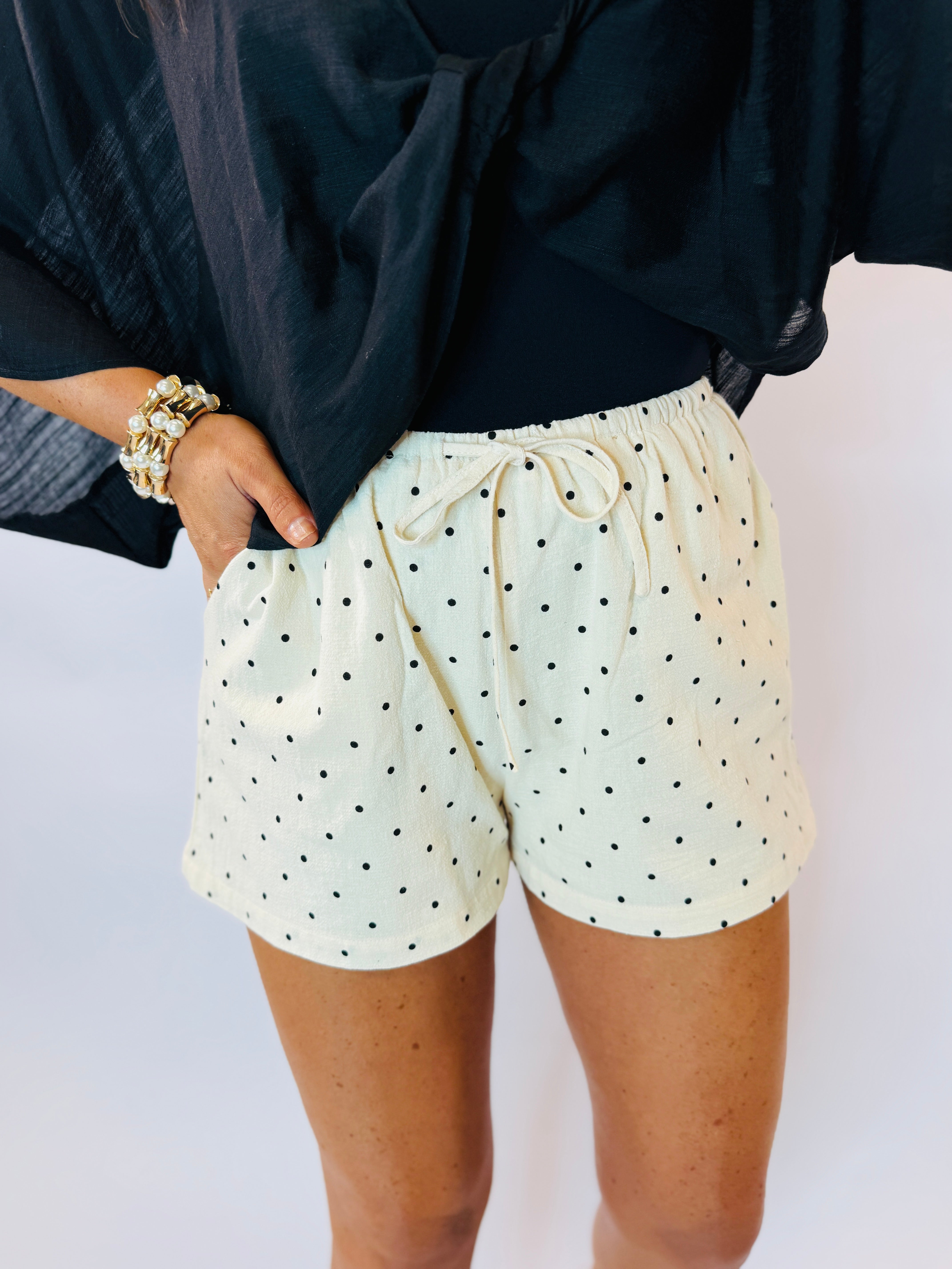 Cream polka dot drawstring shorts with elastic waistband, styled with navy top and gold bracelet.