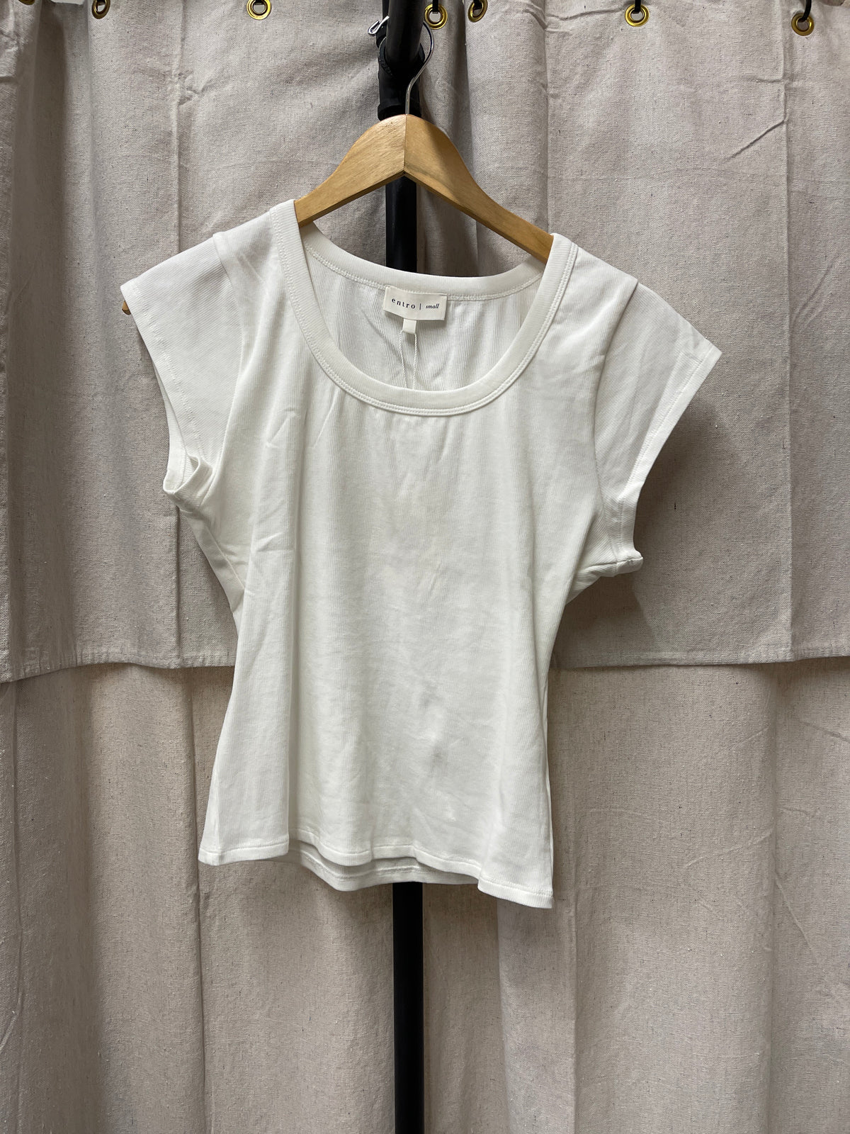 White short-sleeve Rowan top hanging on wooden hanger against neutral fabric backdrop