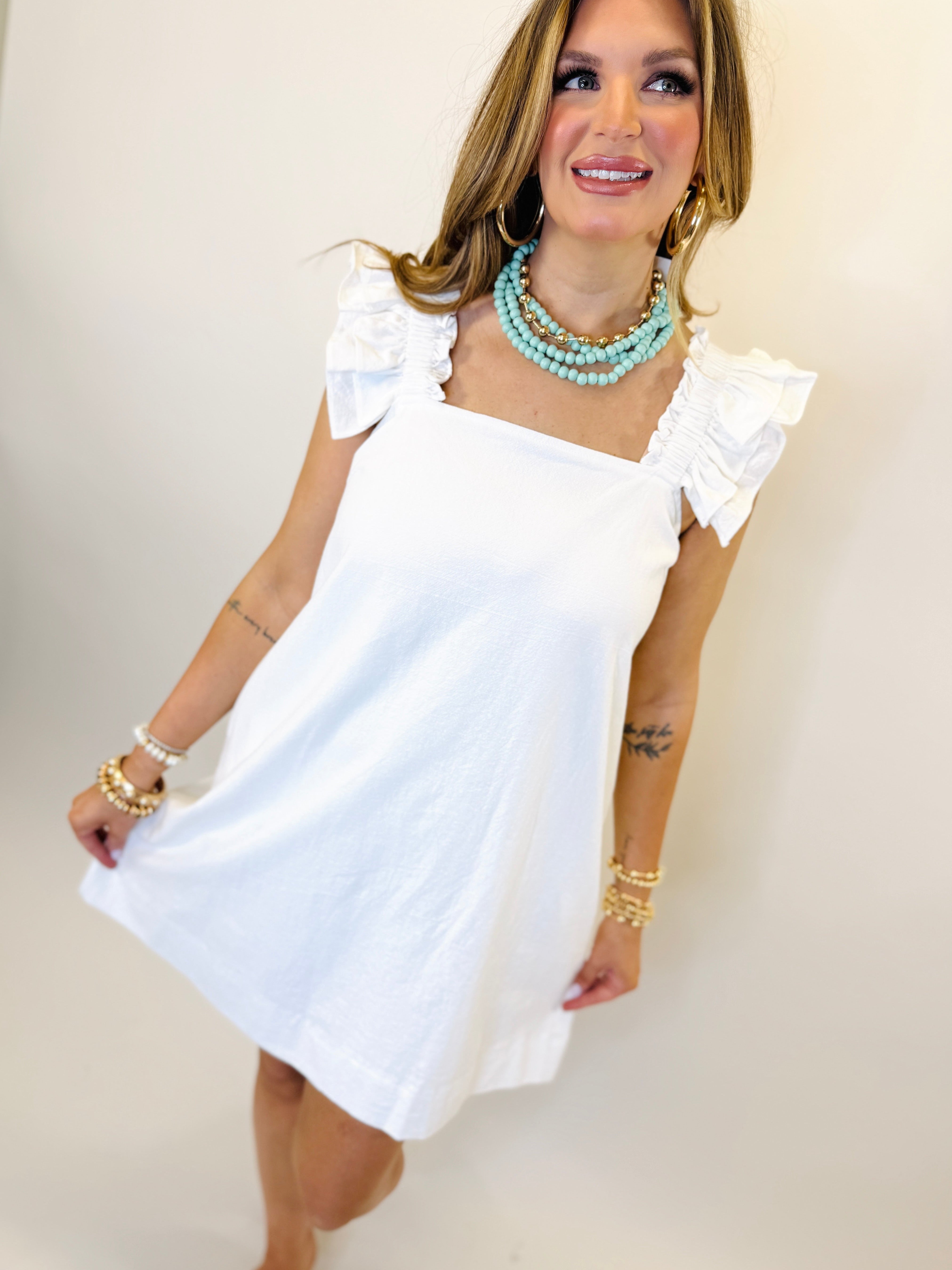Woman wearing white ruffled sleeve mini dress with turquoise statement necklace and gold jewelry accessories.