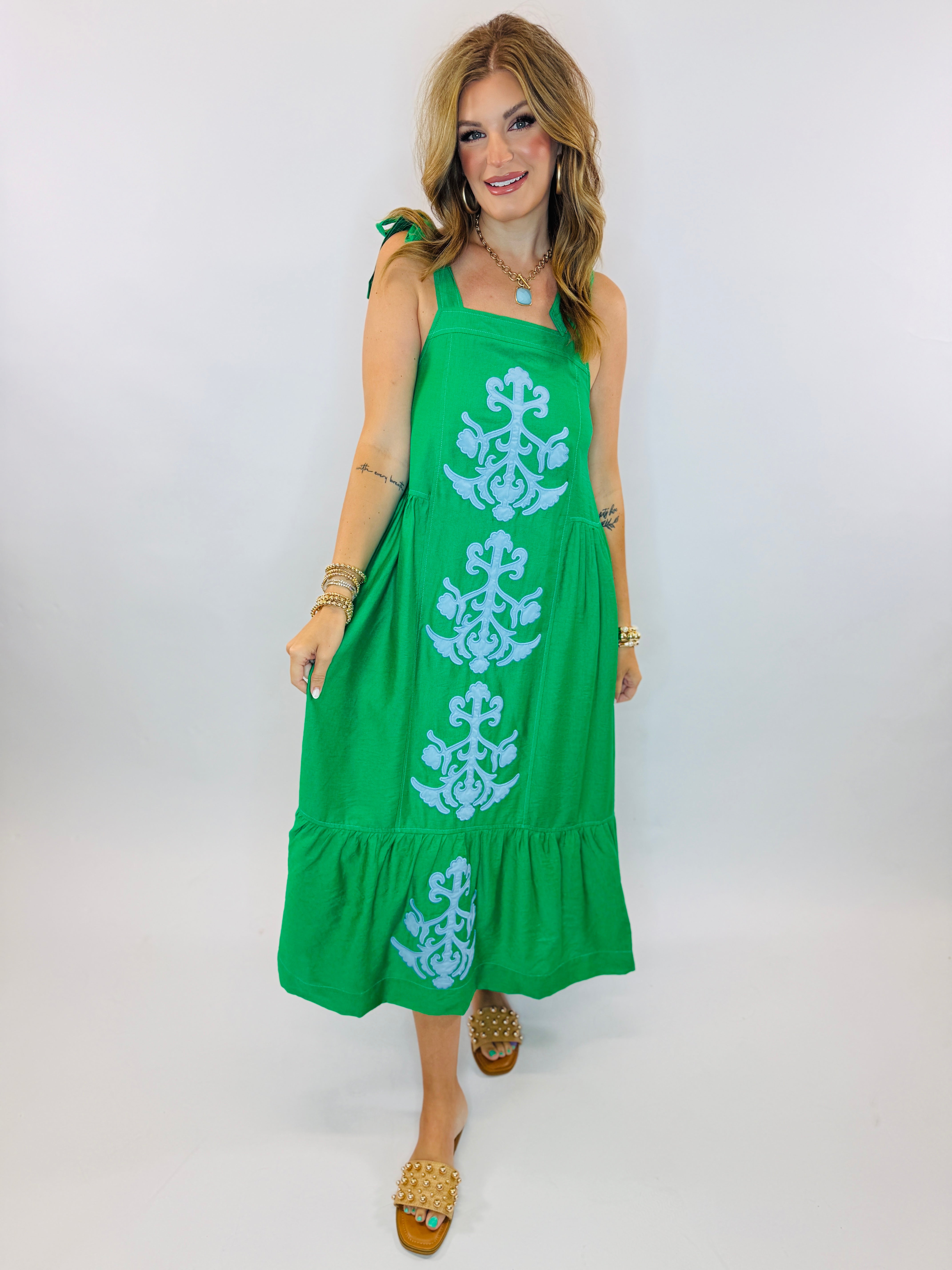 Green midi dress with white embroidered pattern, tie shoulder straps, and tiered ruffle hem