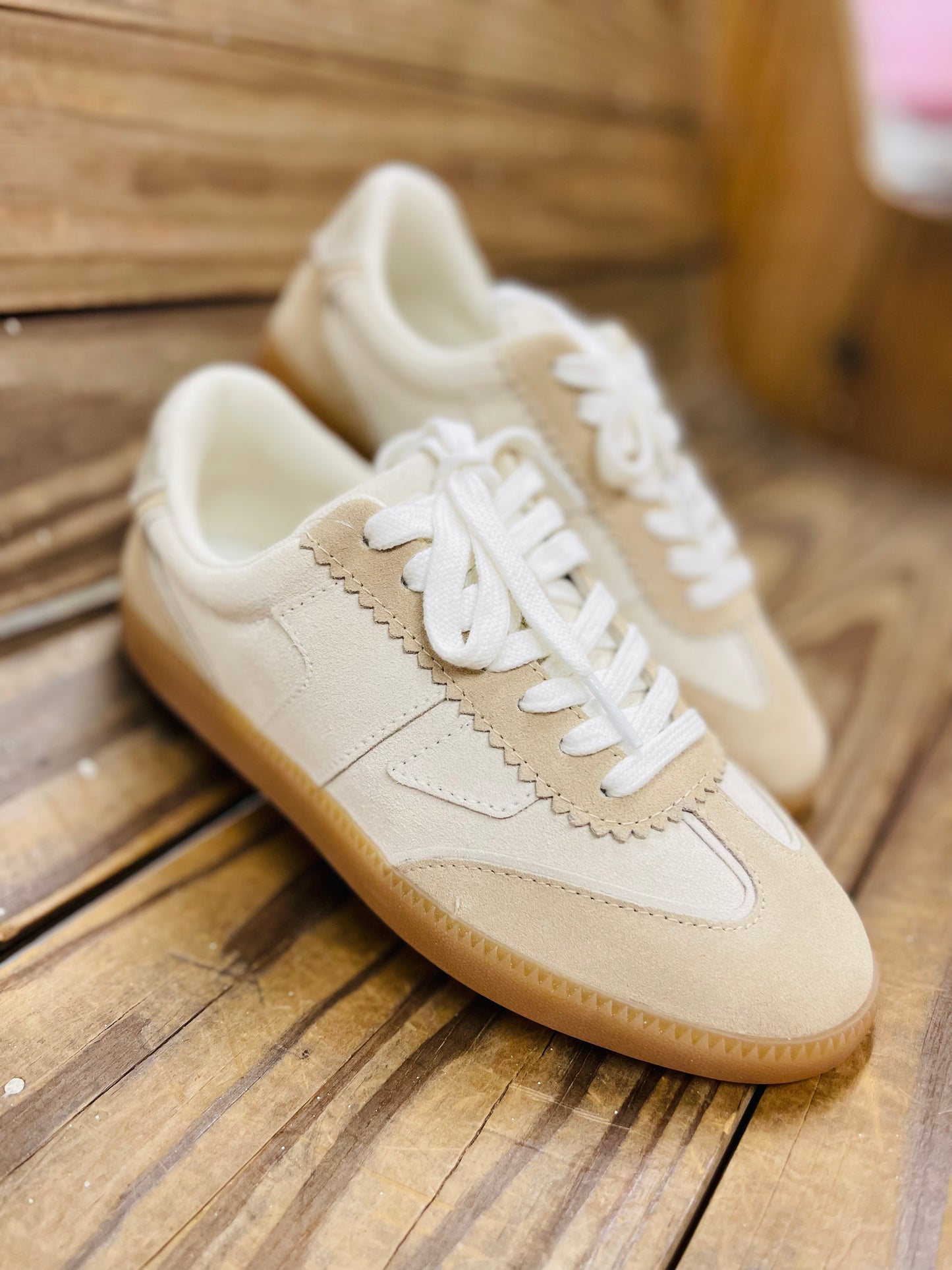 Cream-colored Colins sneakers with white laces and gum sole on wooden surface