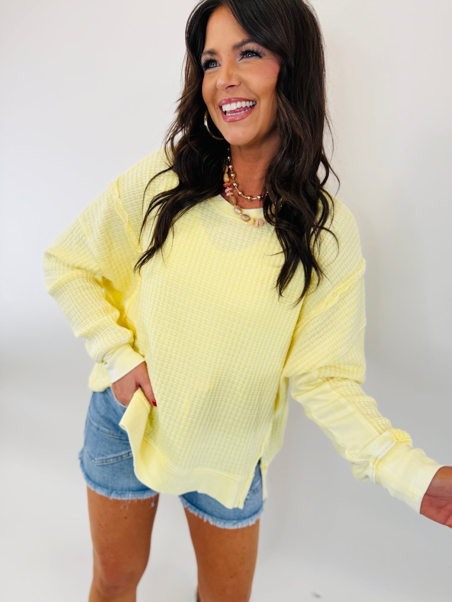 Woman wearing yellow oversized knit sweater with denim shorts, smiling against white background