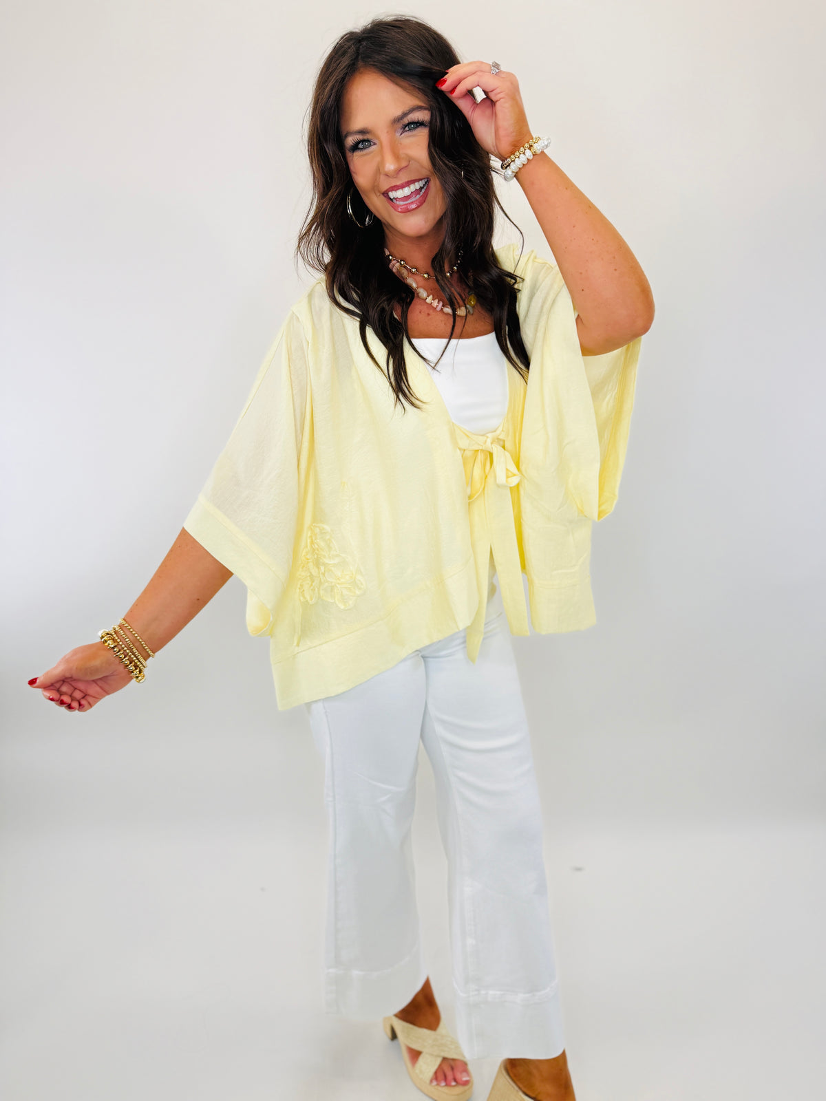 Woman wearing yellow sheer kimono cardigan with tie front over white tank top and white pants