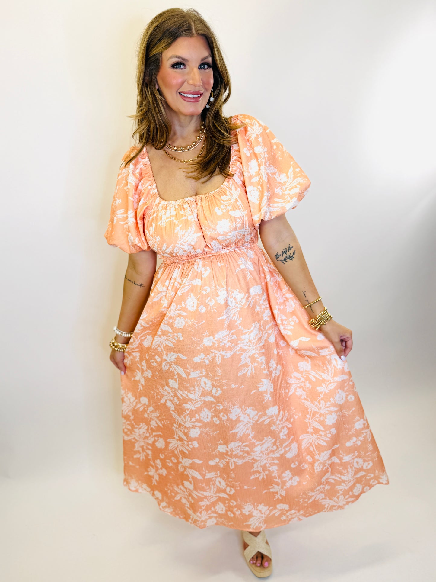 Woman wearing peach floral midi dress with puff sleeves, square neckline, and elastic waist