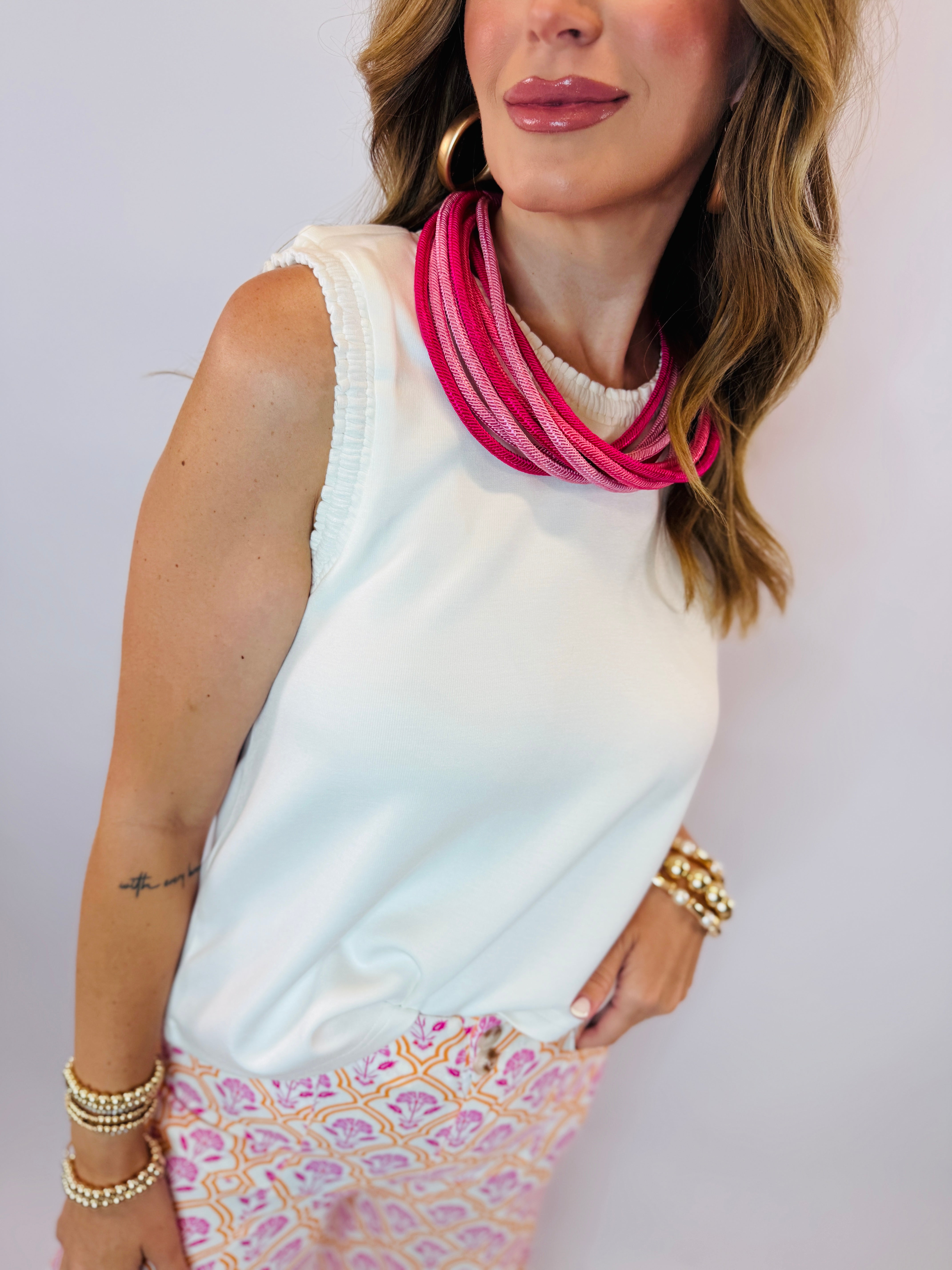 Woman wearing off-white sleeveless Georgie top with pink statement necklace and patterned skirt