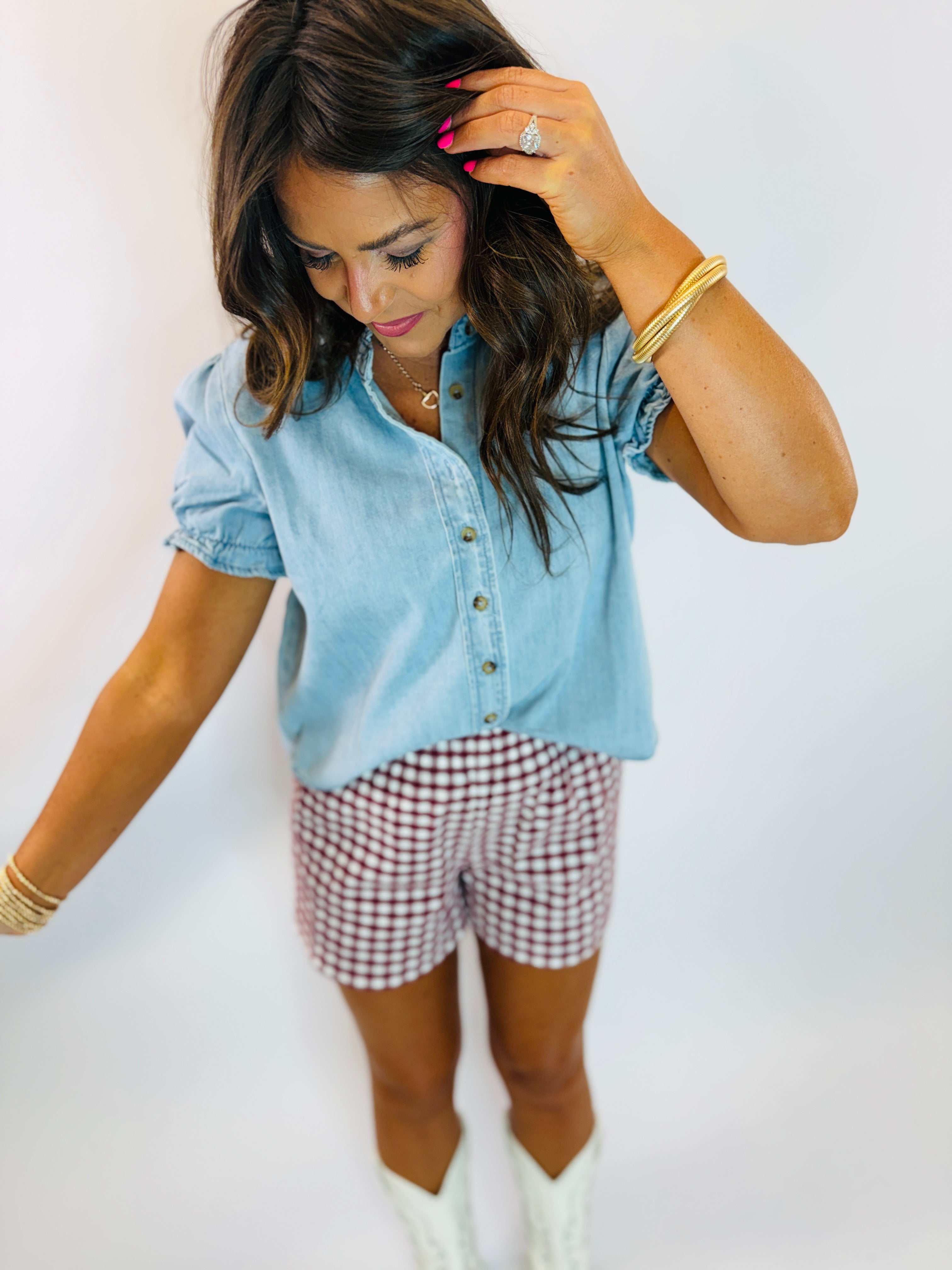 Woman wearing light blue chambray Warren Top with puff sleeves and button-front placket, styled with gingham shorts.