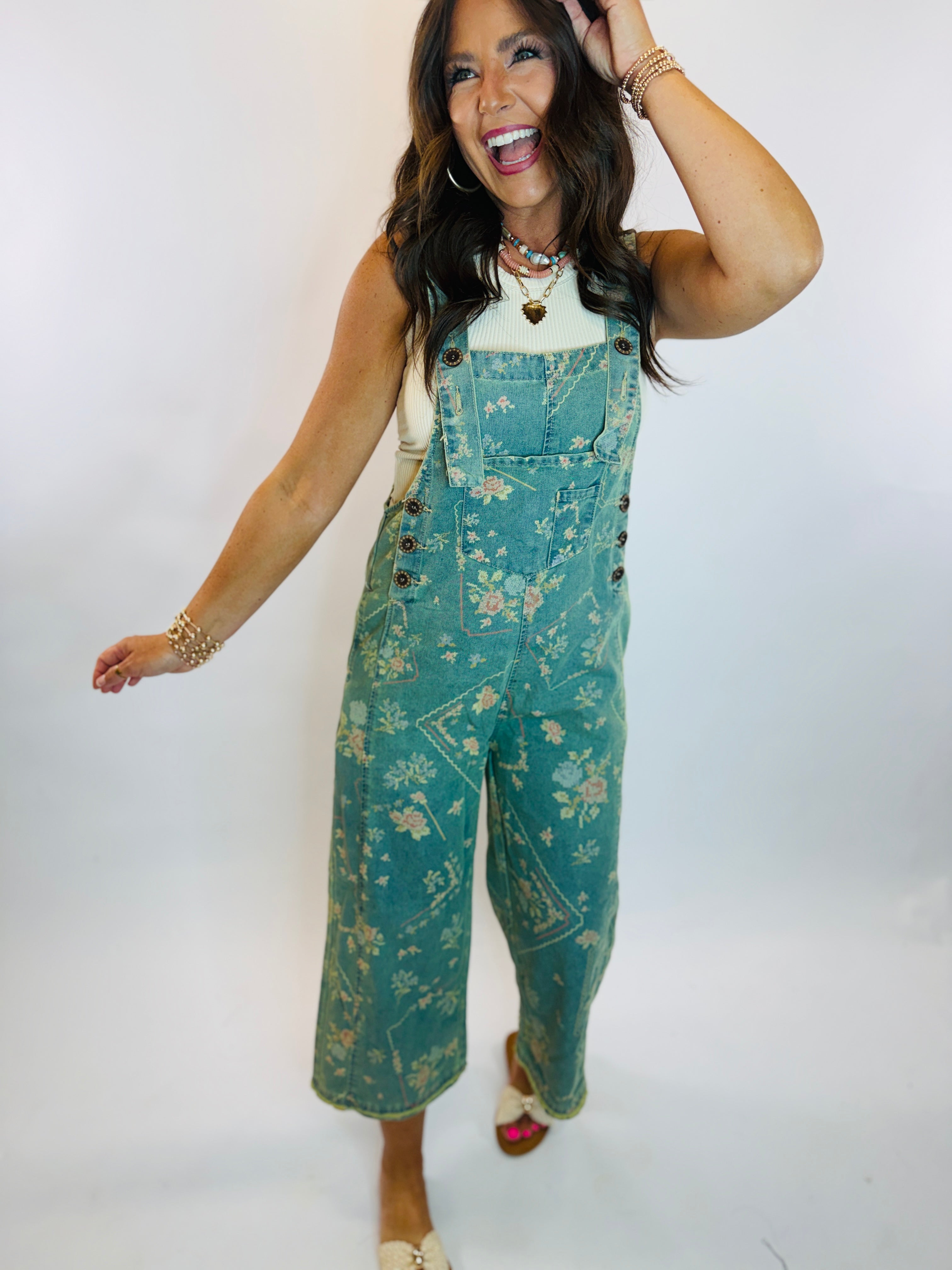 Woman wearing teal floral print wide-leg cropped denim overalls with white ribbed tank underneath.