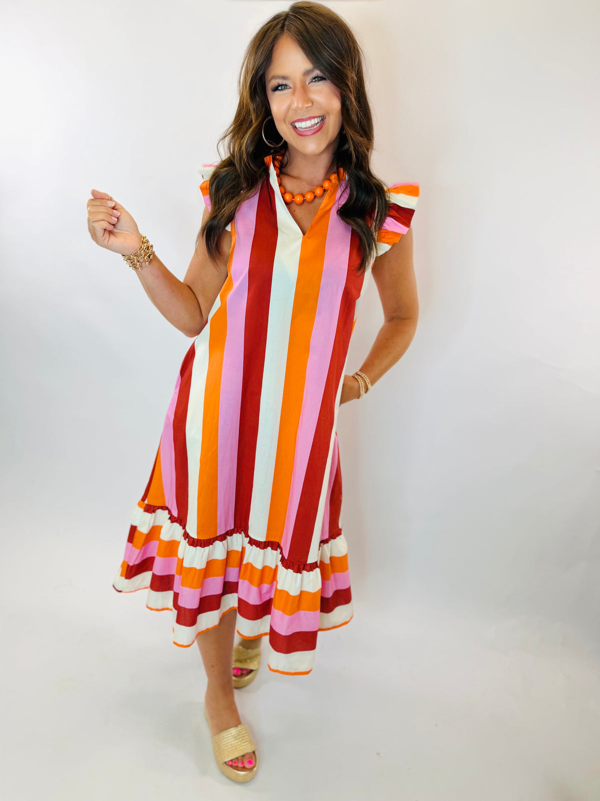 Lola Midi dress with bold multicolor vertical stripes, ruffle hem, and flutter sleeves on smiling model.
