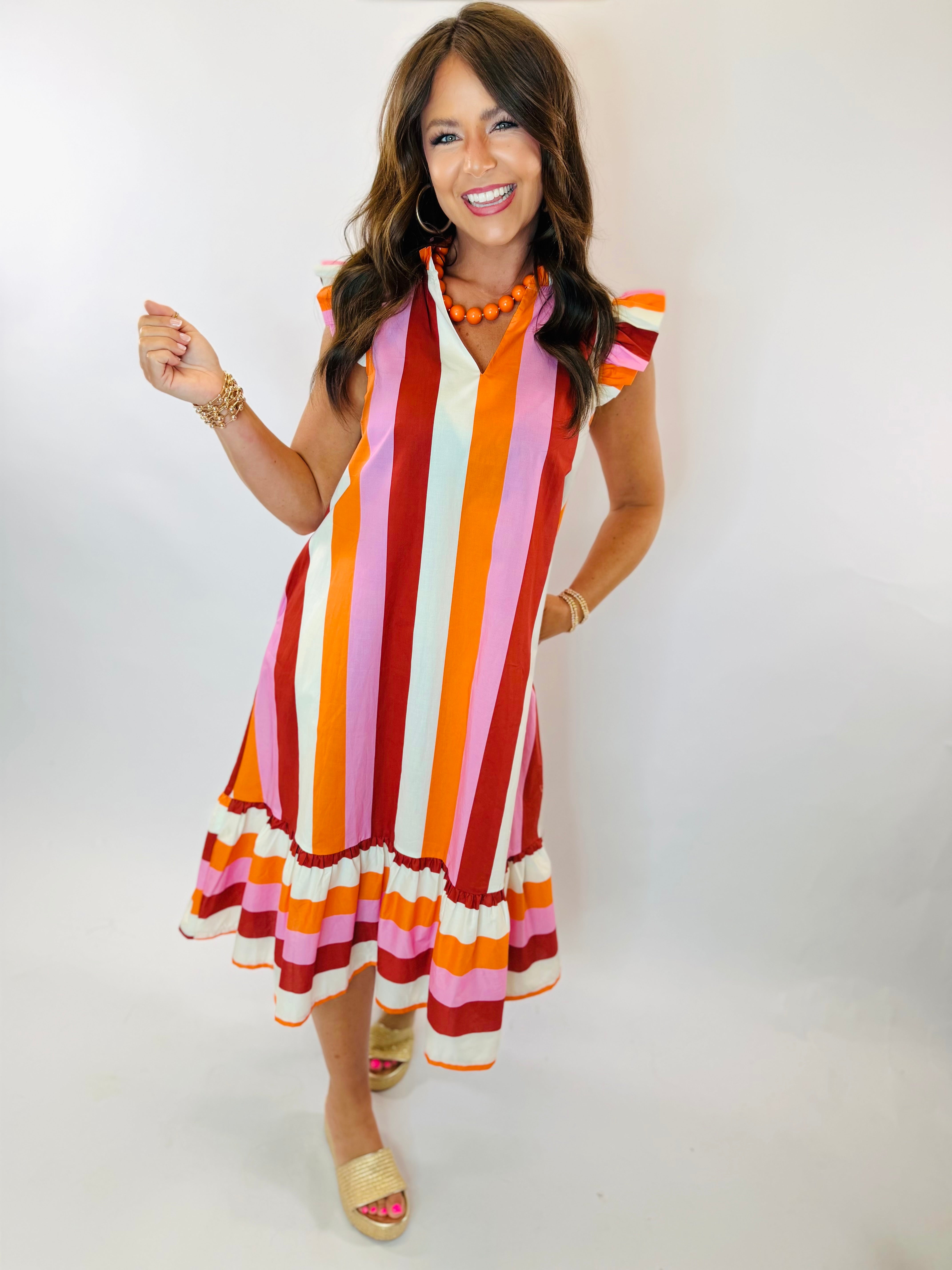 Lola Midi dress with bold multicolor vertical stripes, ruffle hem, and flutter sleeves on smiling model.