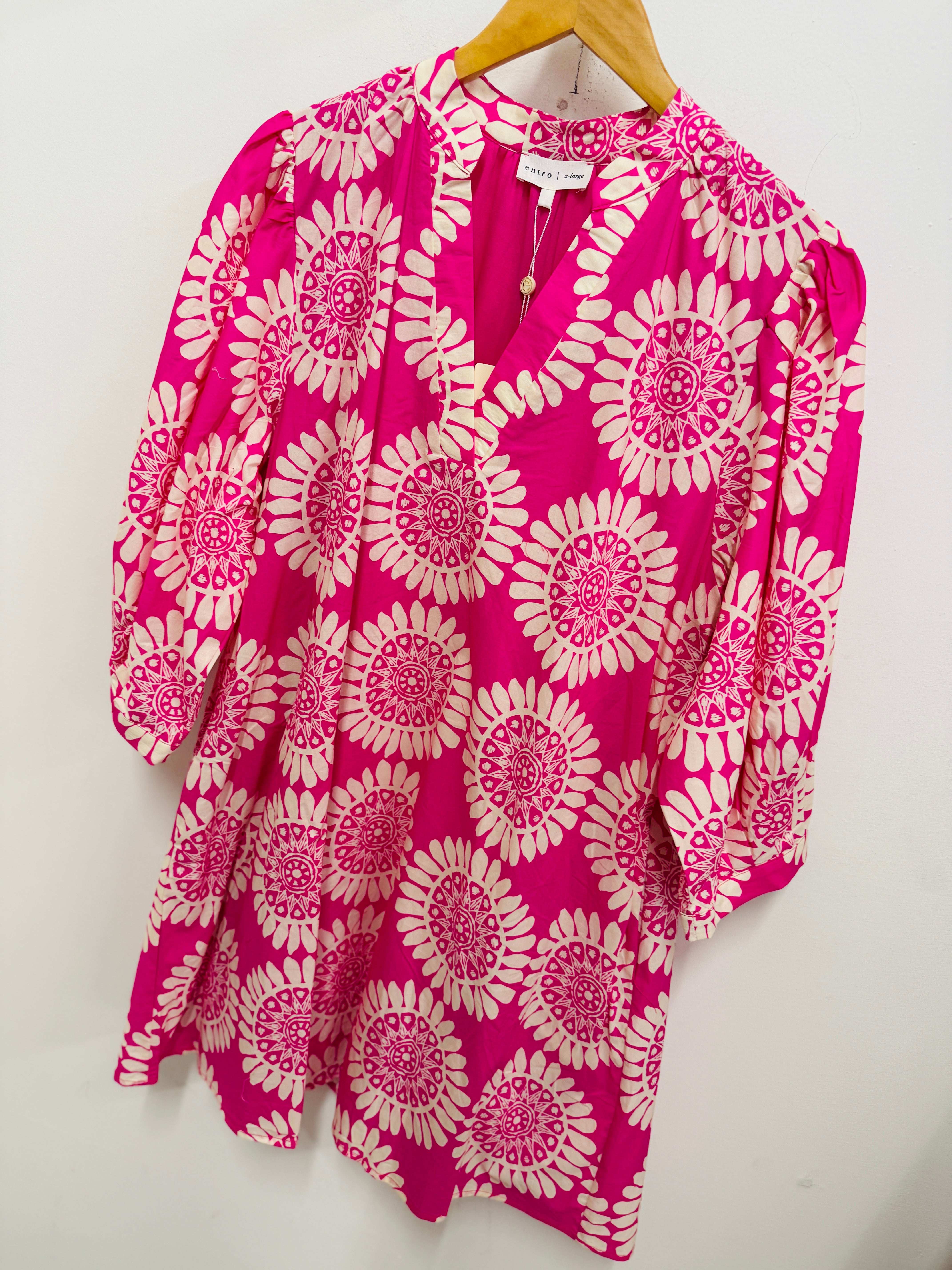 Pink and white floral patterned dress with three-quarter sleeves hanging on wooden hanger against white background.