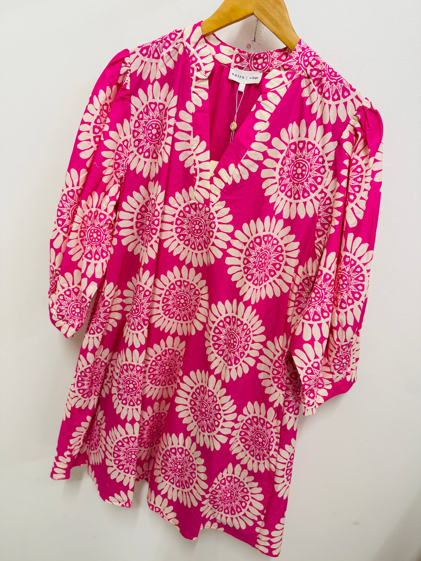 Pink and white floral patterned dress with three-quarter sleeves hanging on wooden hanger against white background.