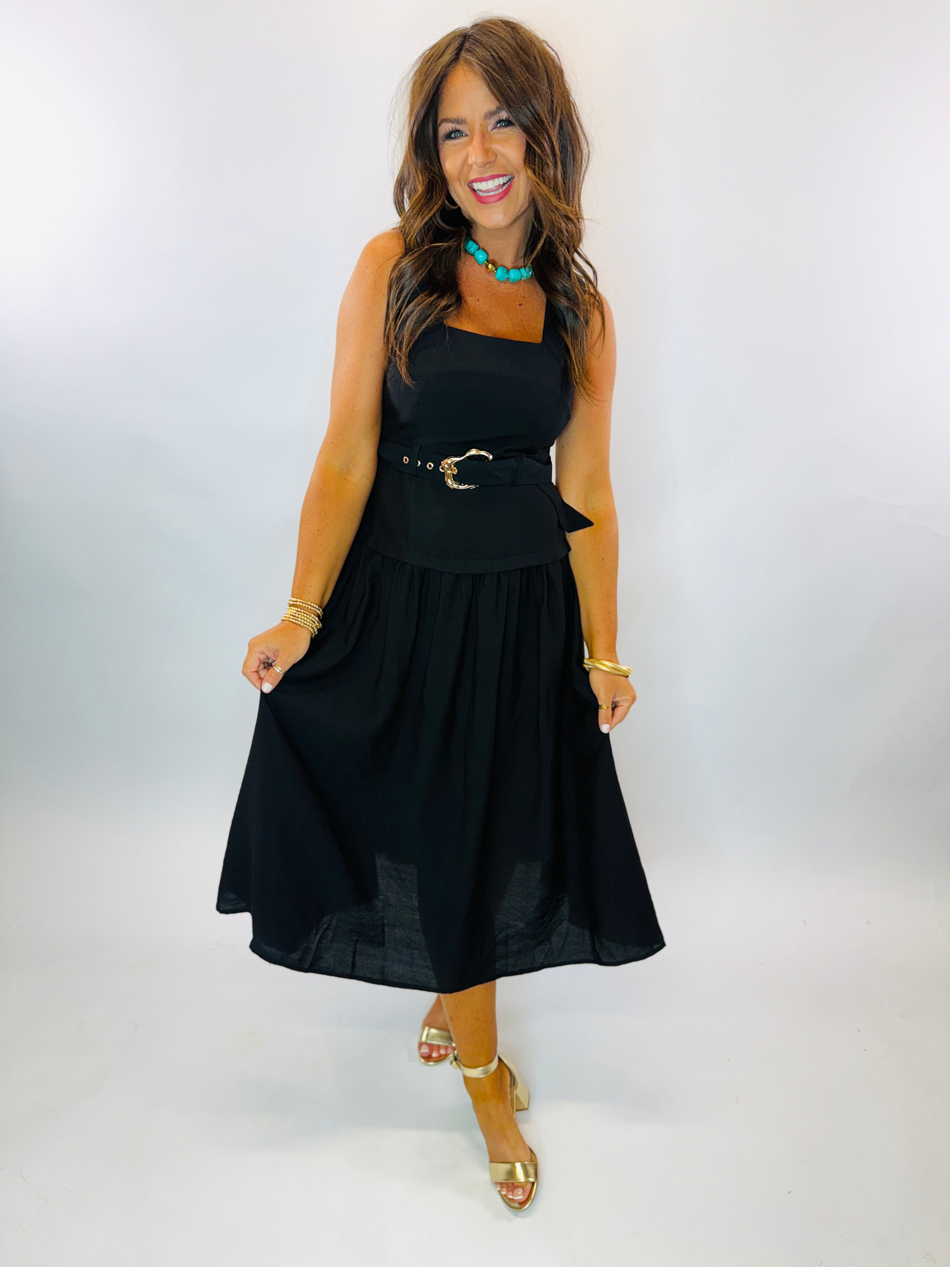 Woman wearing black midi Daniella Dress with gold belt buckle, turquoise necklace, and gold heels.