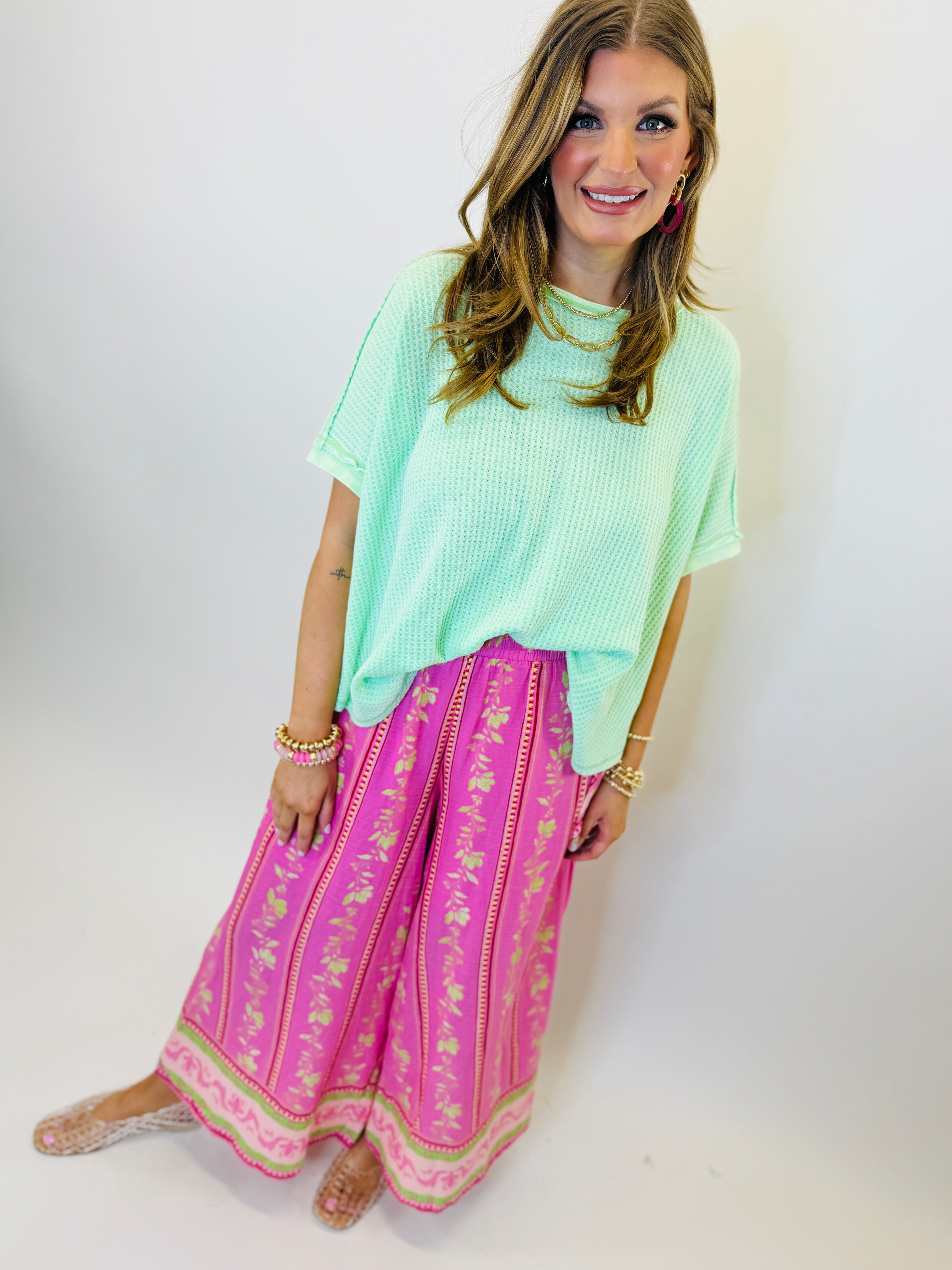 Woman wearing mint green short-sleeve Mikaela top with textured fabric, paired with pink patterned maxi skirt