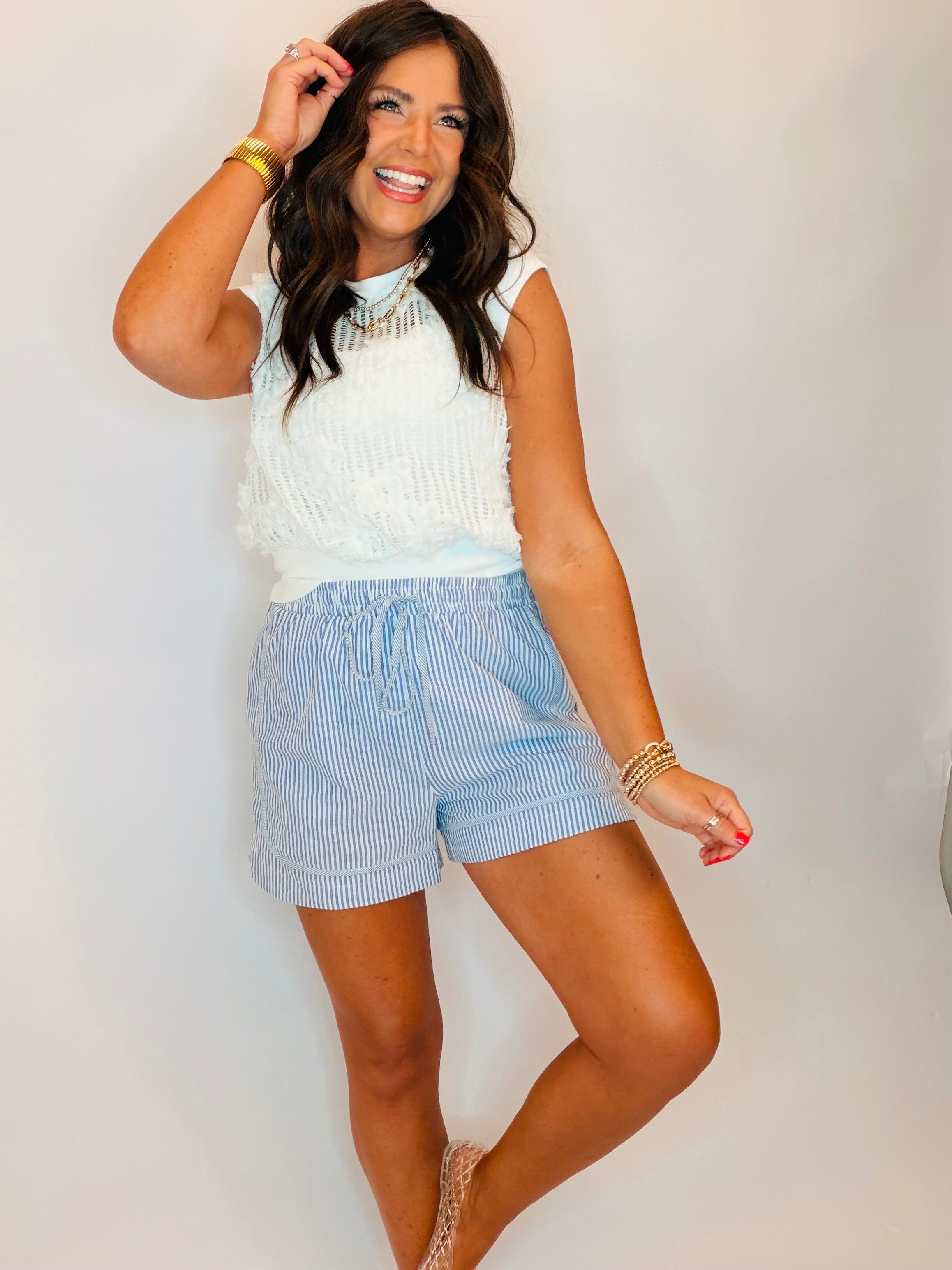 Woman wearing blue and white striped drawstring shorts with white crochet top and gold jewelry accessories.