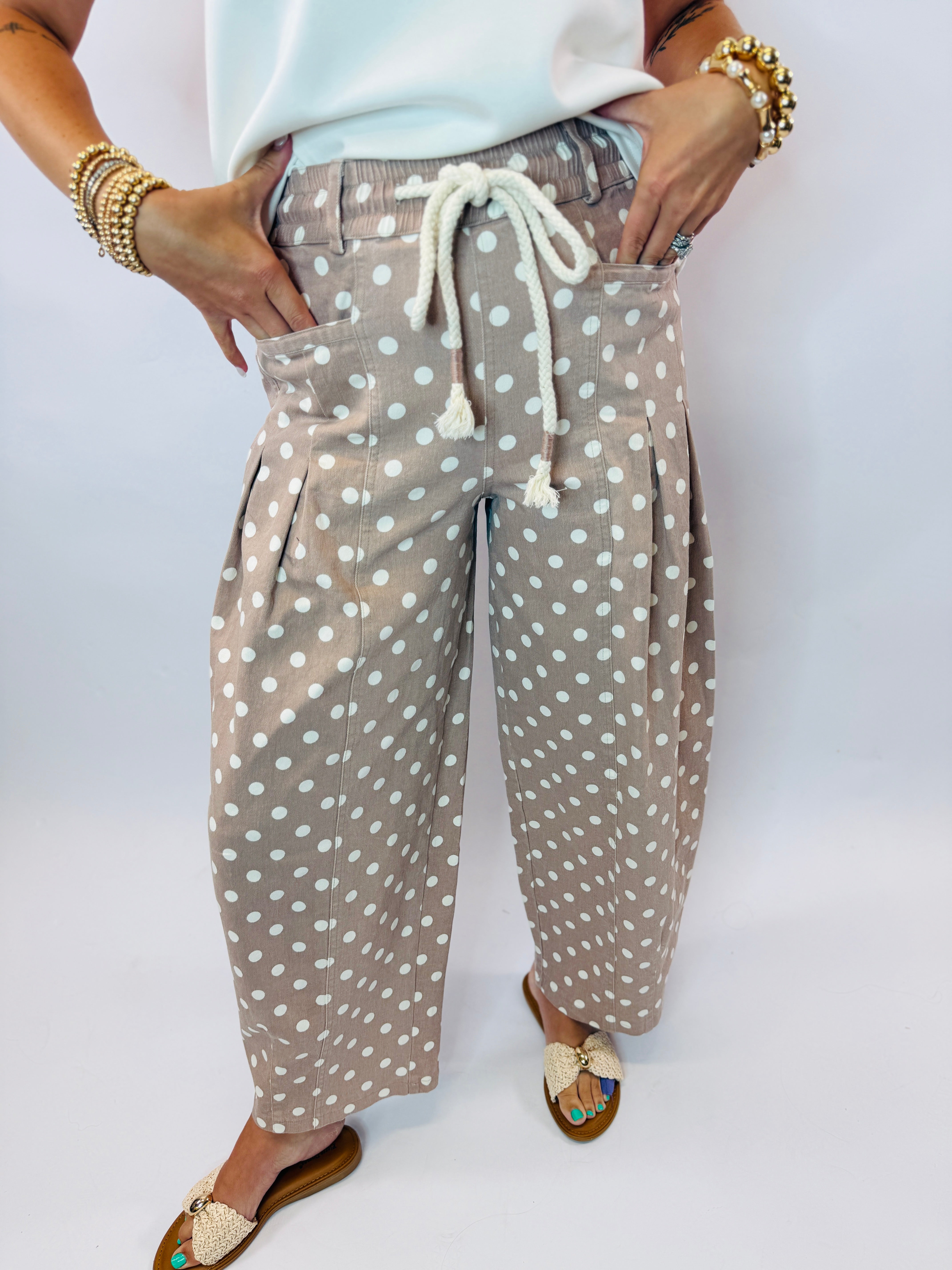Taupe polka dot barrel pants with white drawstring tie and relaxed fit, styled with gold jewelry and sandals.