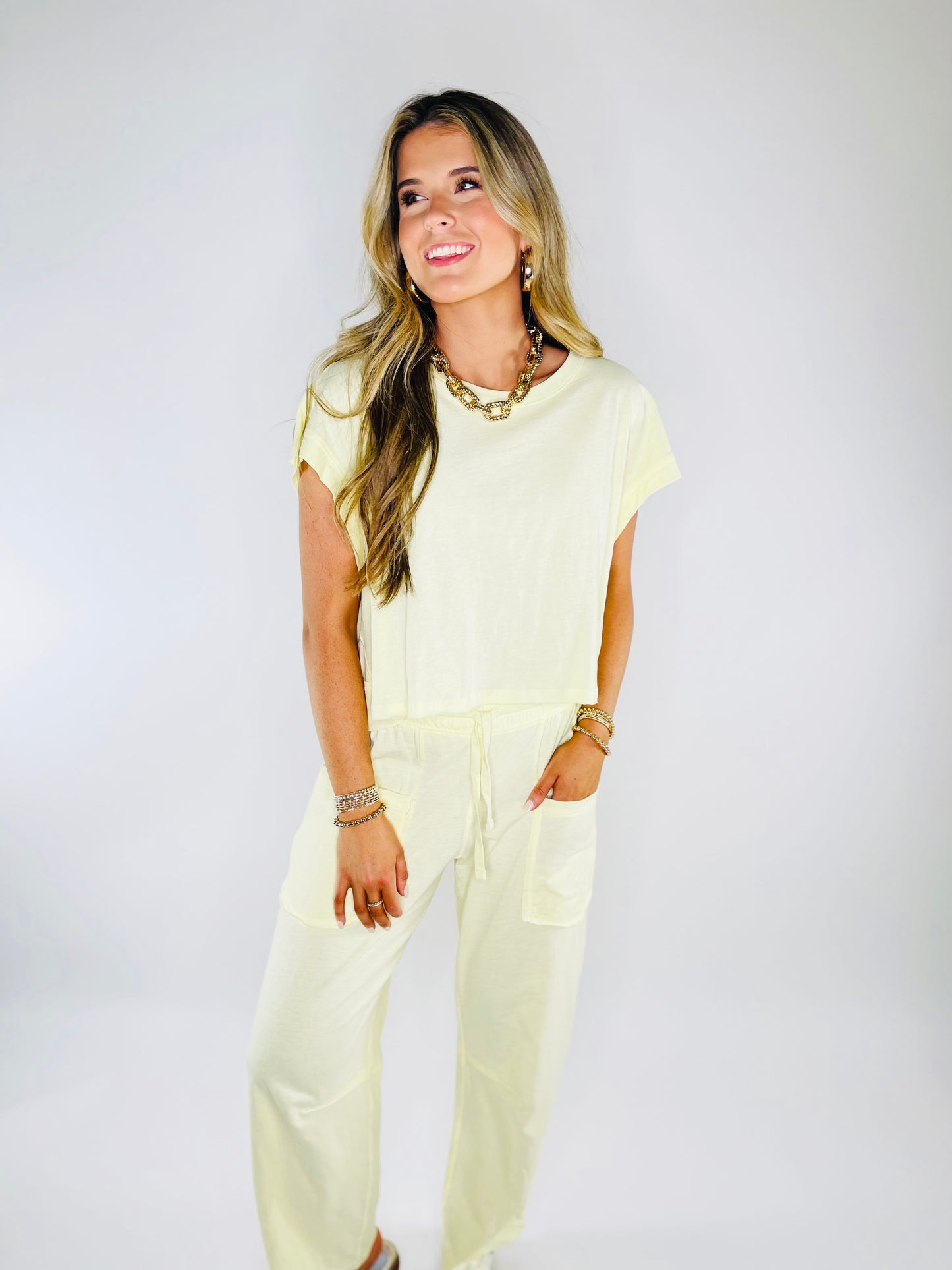 Woman wearing pale yellow relaxed fit short-sleeve top with gold chain necklace and bracelets