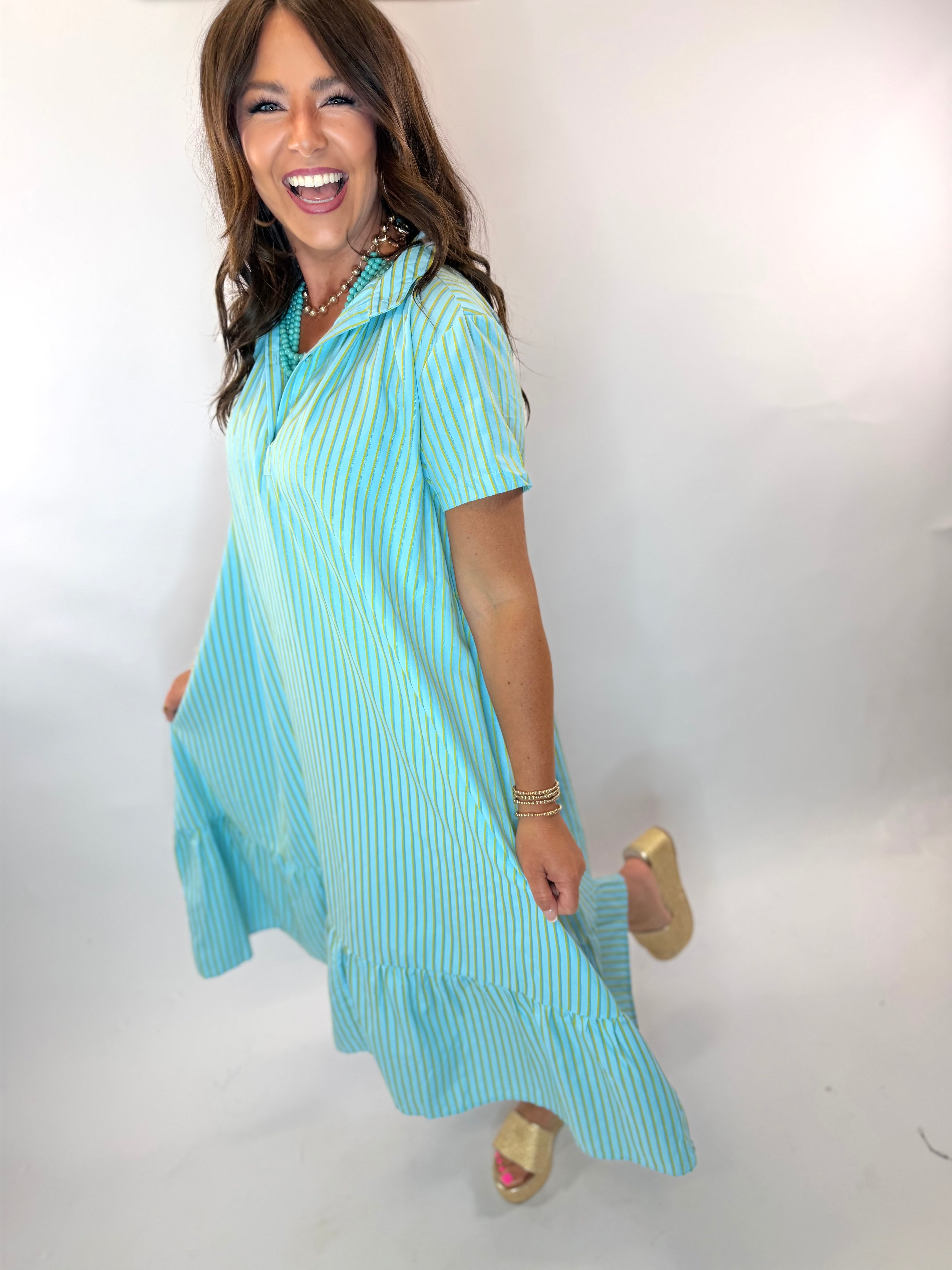 Woman wearing Kate Midi Dress in turquoise and gold stripe with ruffle hem and collar.