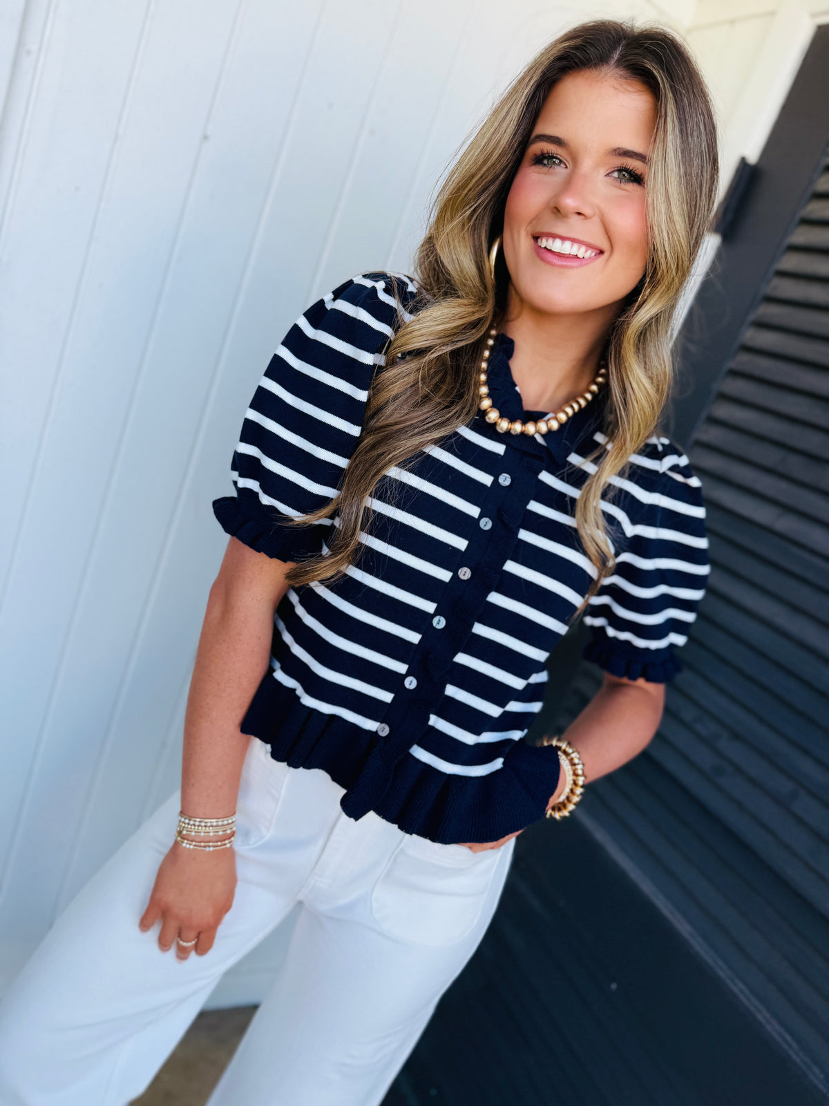 Woman wearing navy and white striped cardigan sweater with pearl necklace and white pants