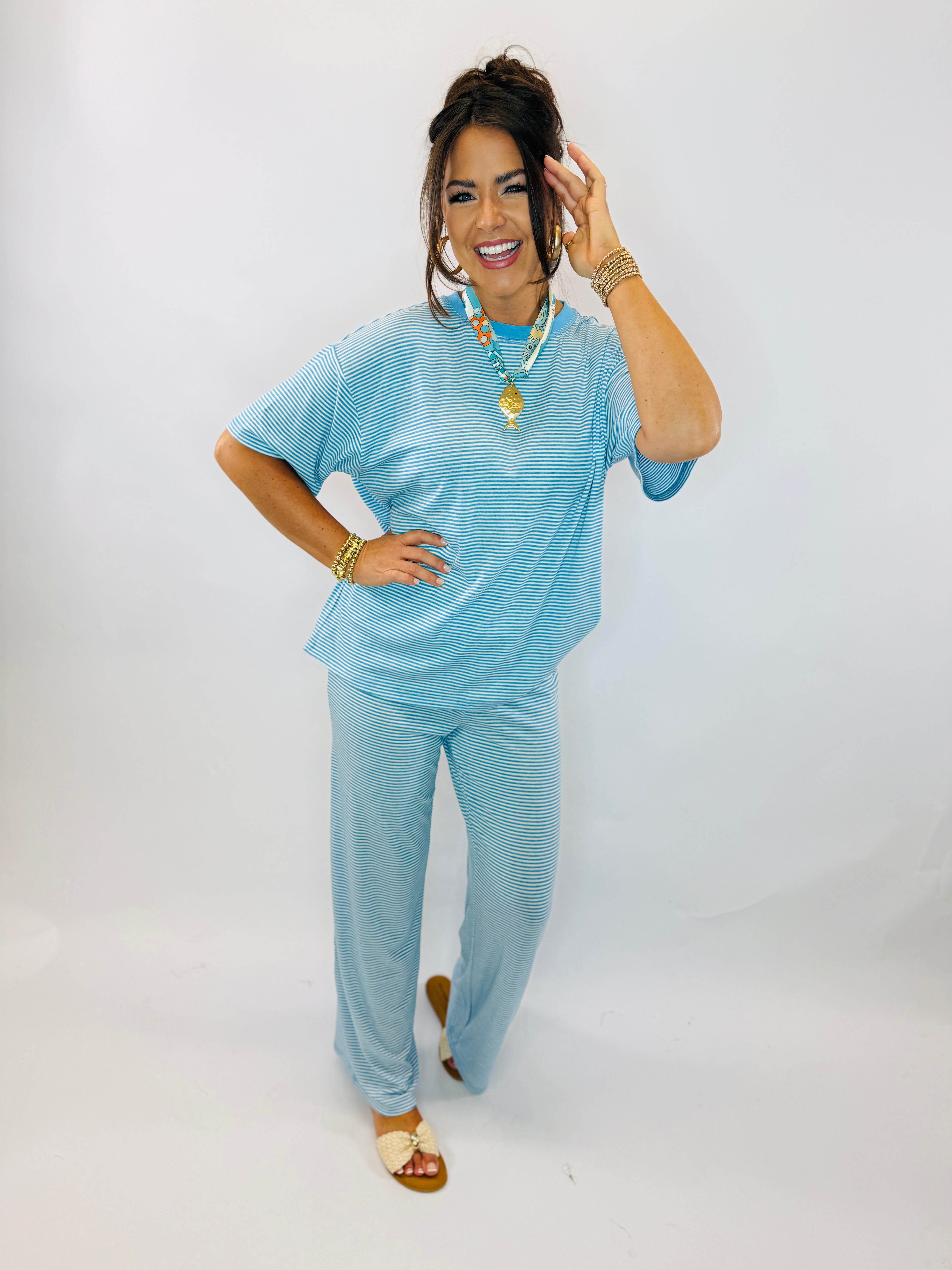 Woman wearing blue striped matching top and pants set with gold jewelry and sandals, smiling and posing.