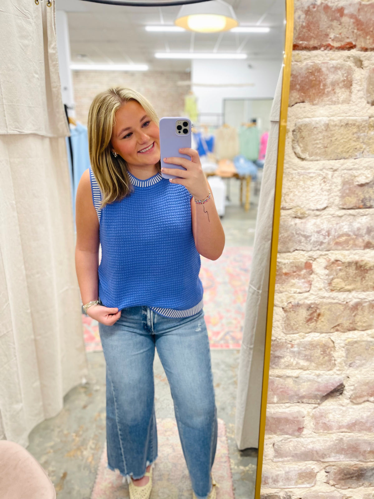 Woman wearing blue knit sleeveless top and light wash wide leg denim jeans taking mirror selfie