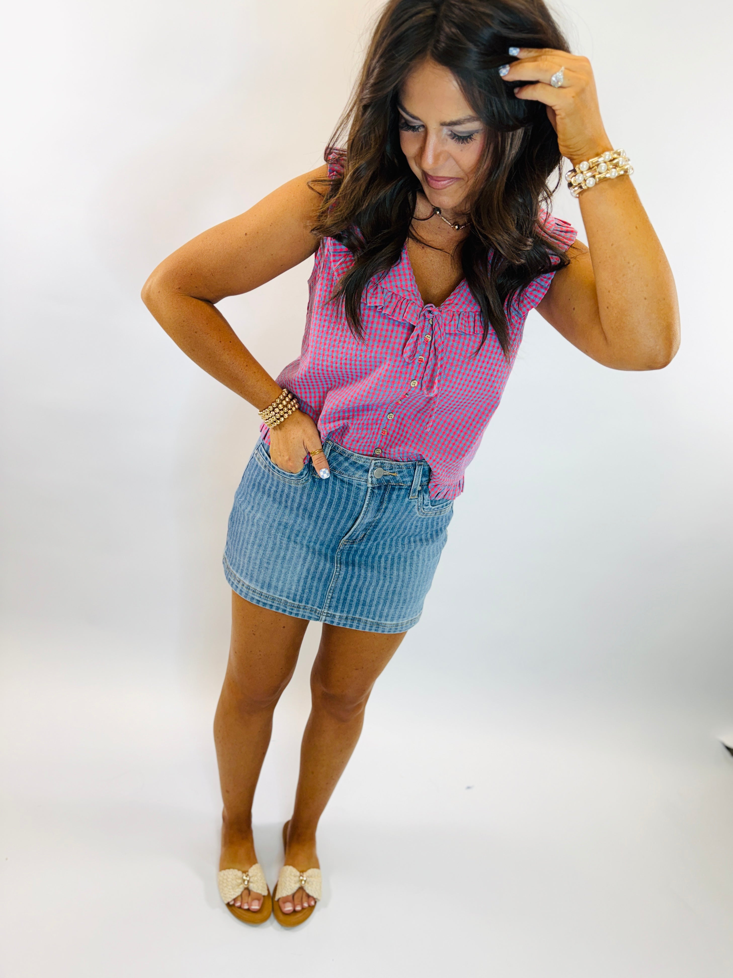 Woman wearing pink and blue gingham sleeveless tank top with lace-up neckline, paired with denim skirt