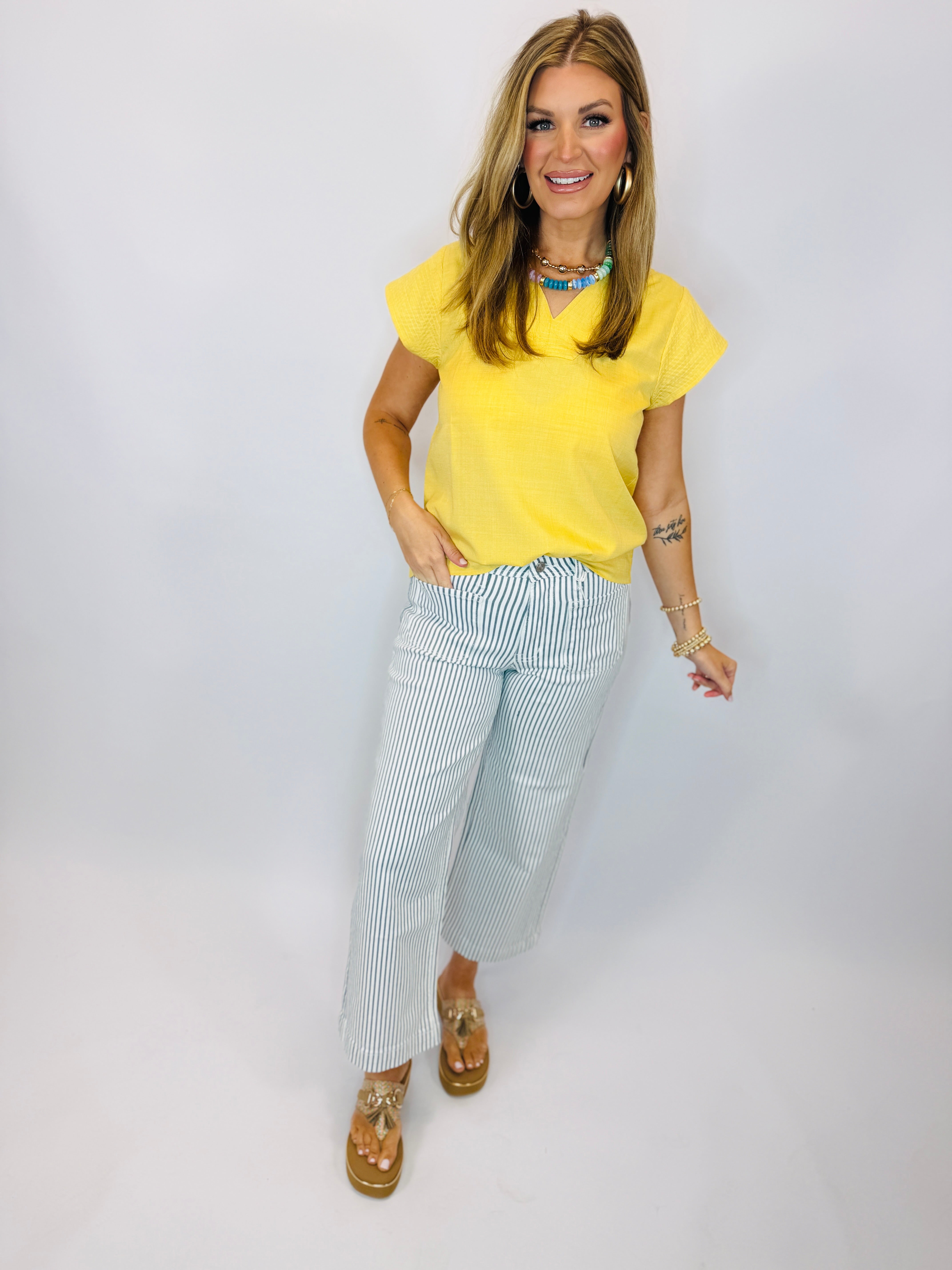 Woman wearing yellow Tracy Tank top with blue and white striped pants and gold sandals