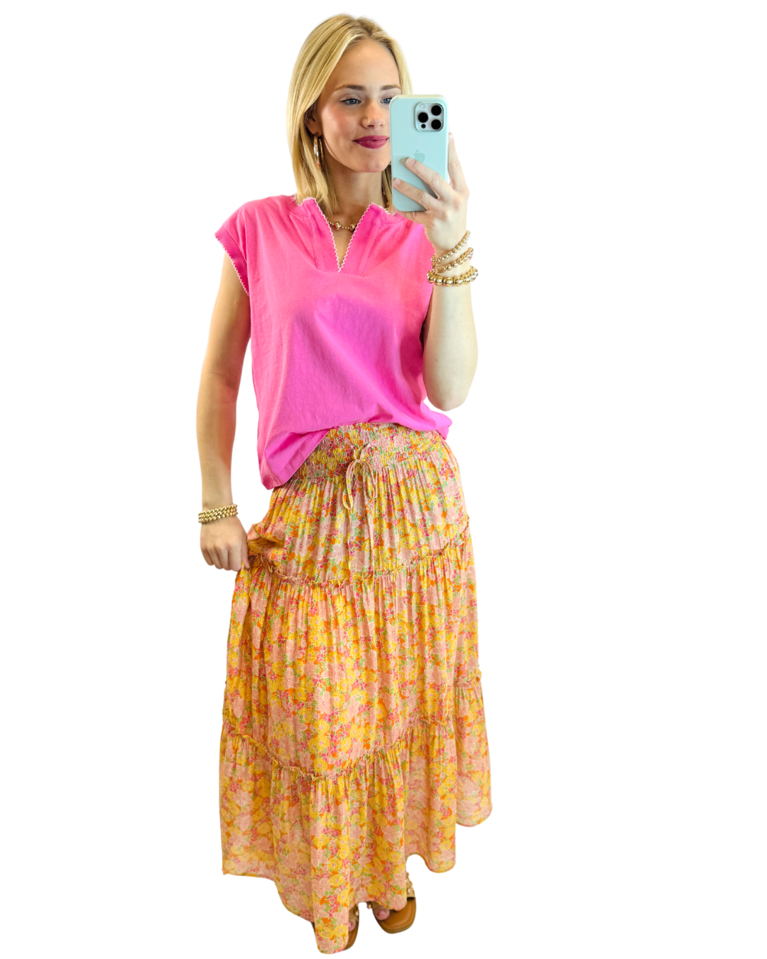 Woman wearing bright pink Taylor Tee with floral tiered maxi skirt, taking mirror selfie with gold jewelry accessories.
