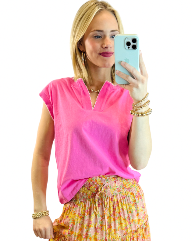 Woman wearing bright pink short-sleeve v-neck tee with floral print skirt, taking mirror selfie