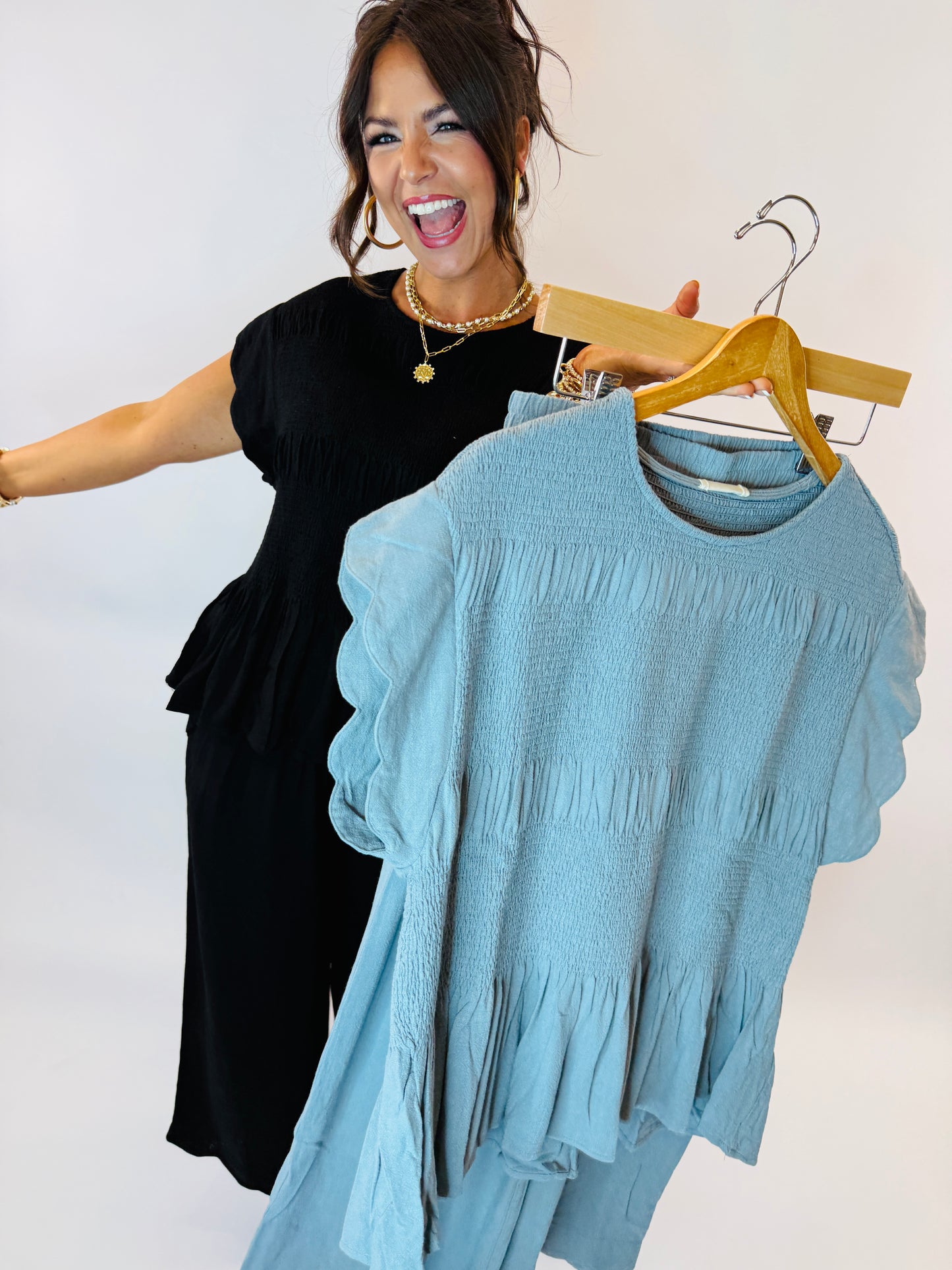 Woman in black dress holding wooden hanger with blue tiered smocked top with ruffle sleeves