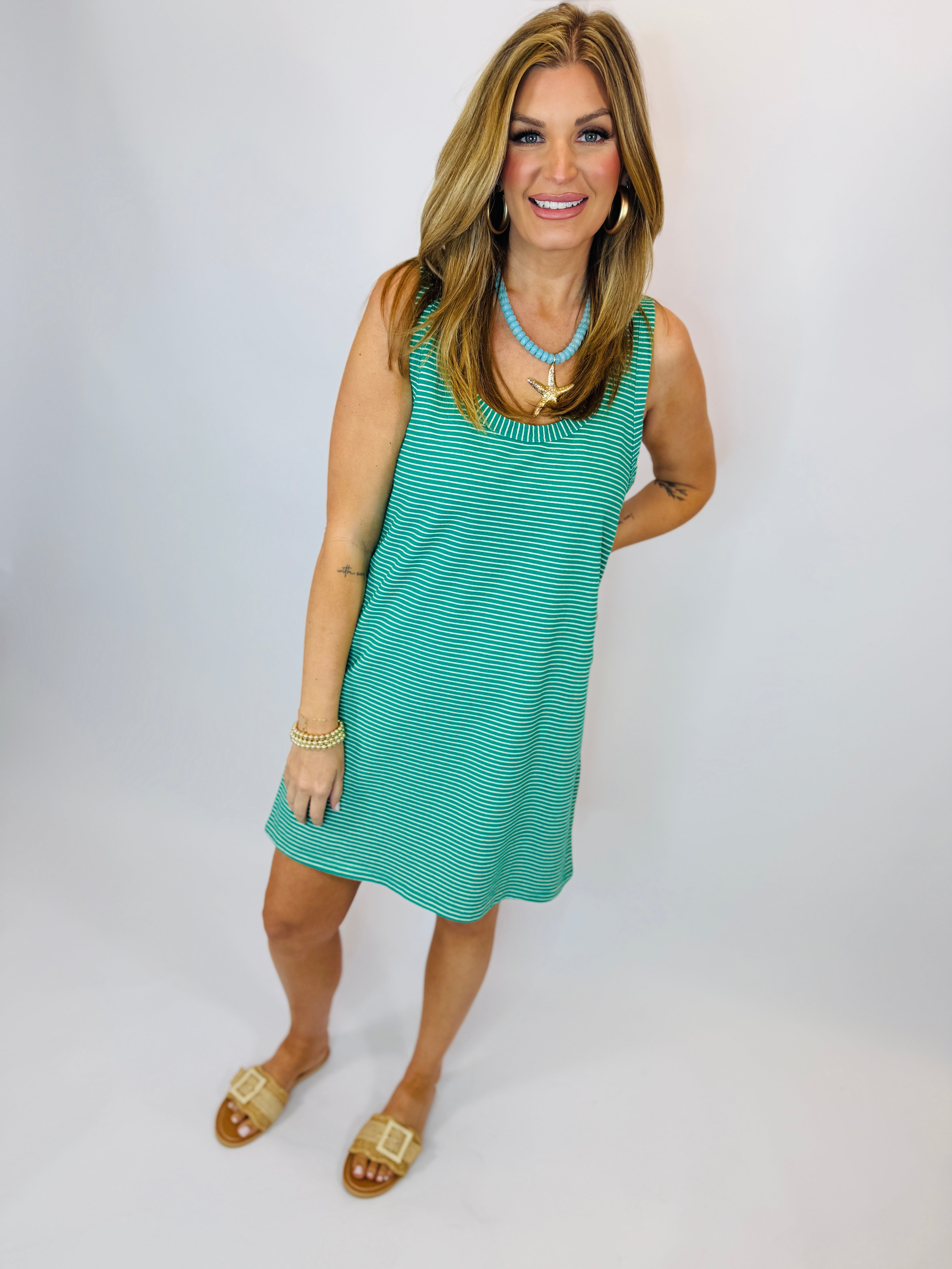 Woman wearing turquoise and white striped sleeveless tank dress with beaded necklace and gold sandals