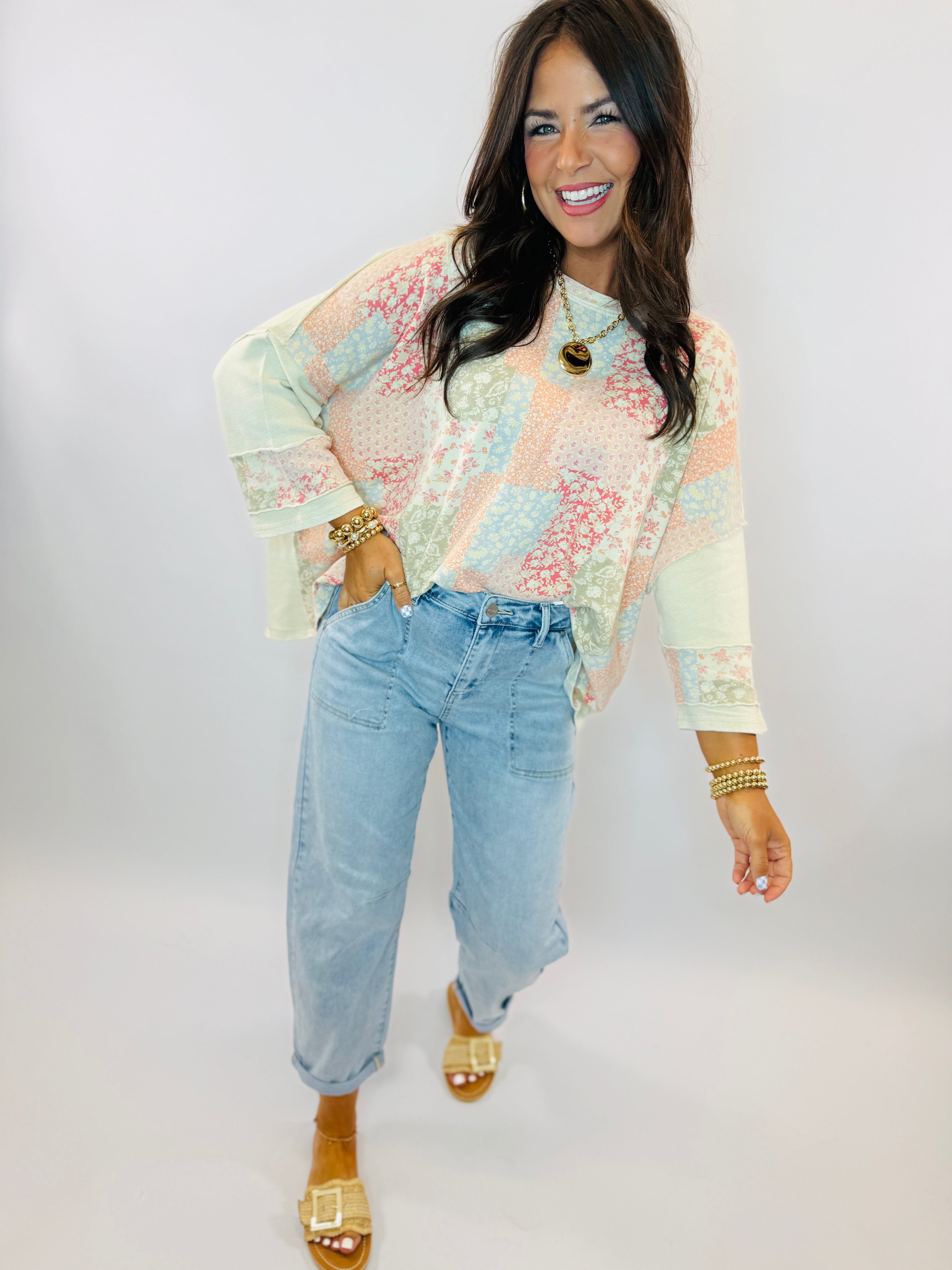 Woman wearing pastel floral Ellie top with sheer sleeves and light wash jeans, styled with gold accessories.