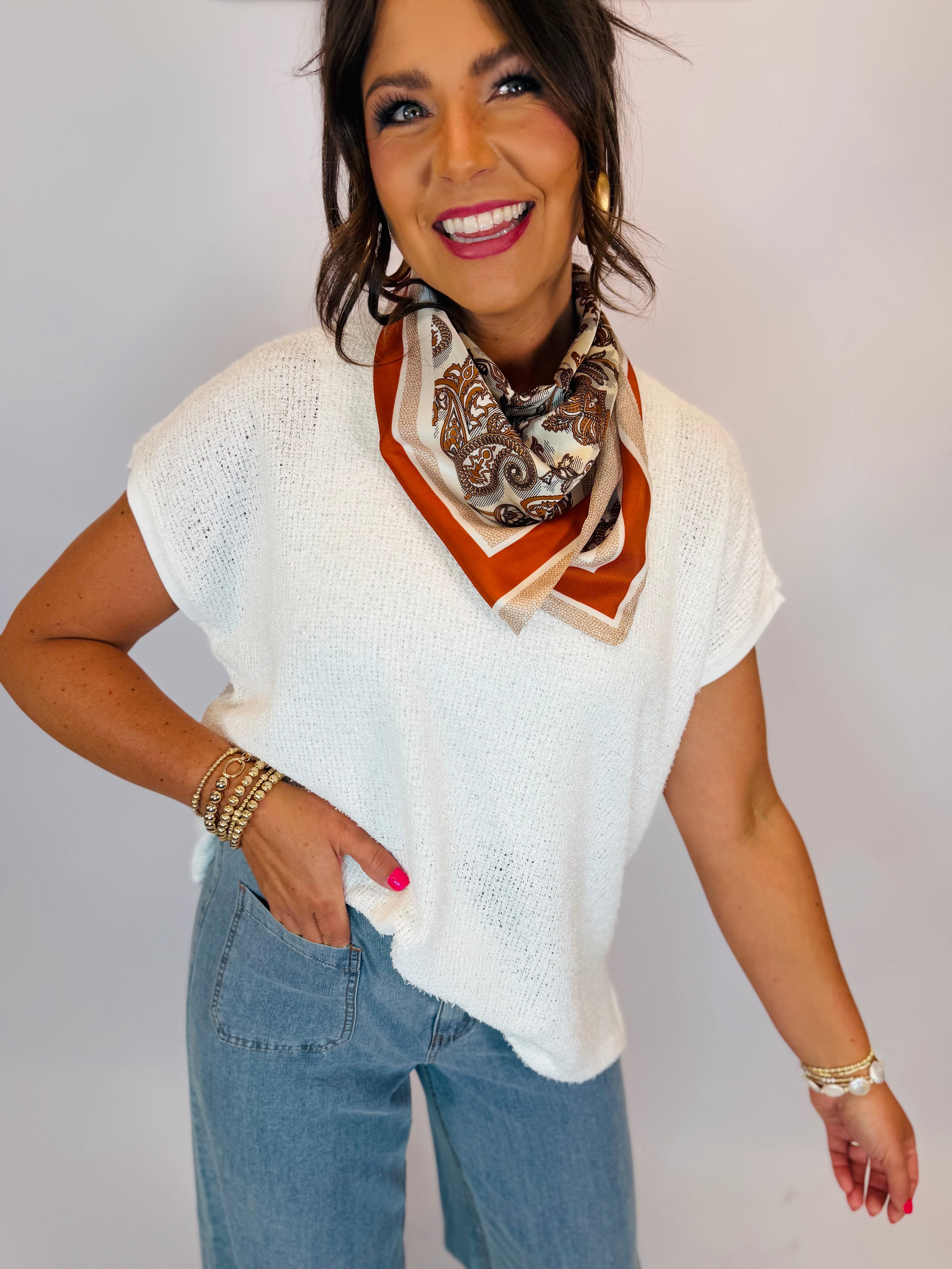 White short-sleeve knit sweater top styled with paisley neck scarf and light wash jeans.