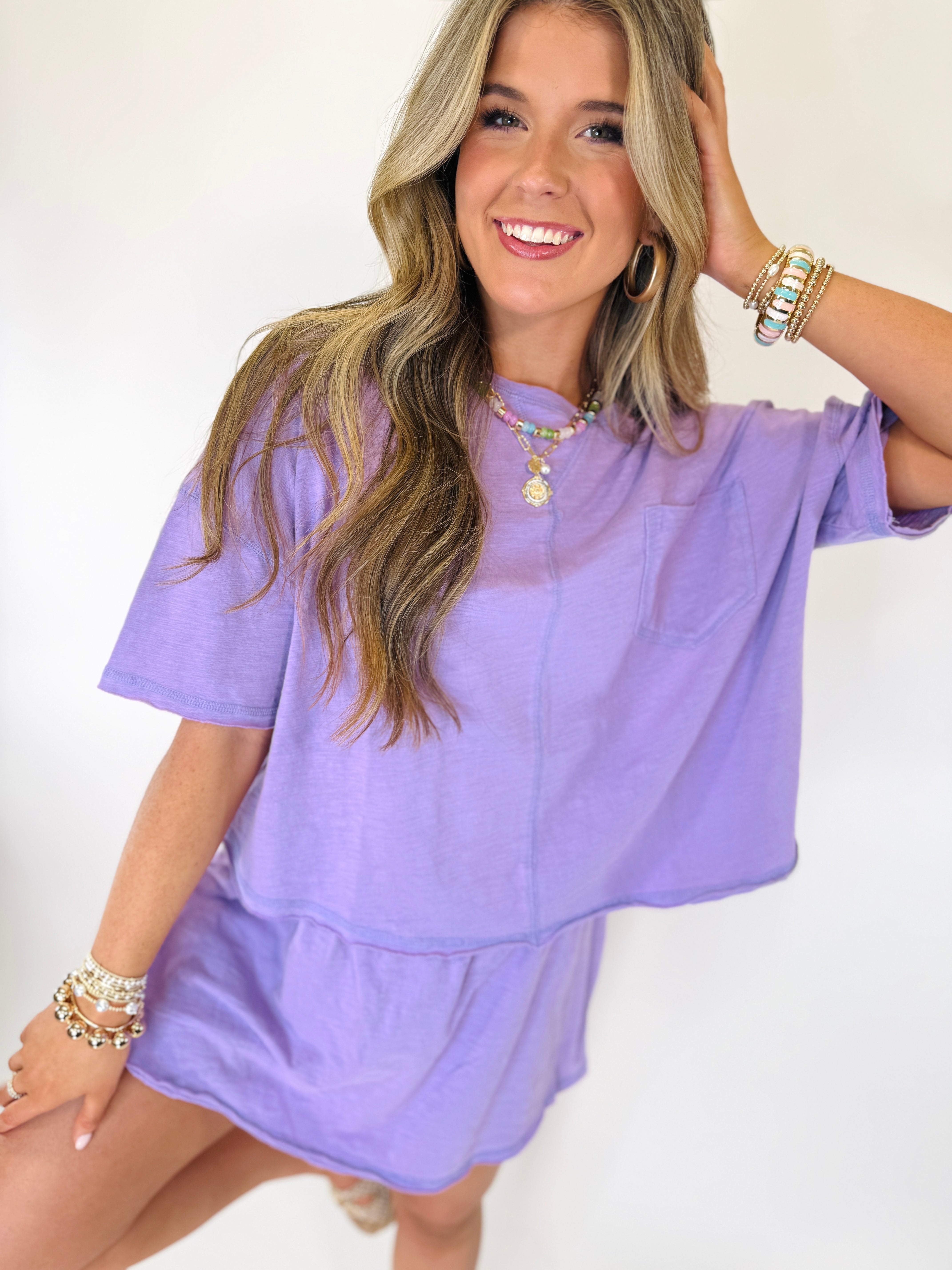 Woman wearing purple oversized t-shirt and matching shorts set, styled with layered jewelry and bracelets.