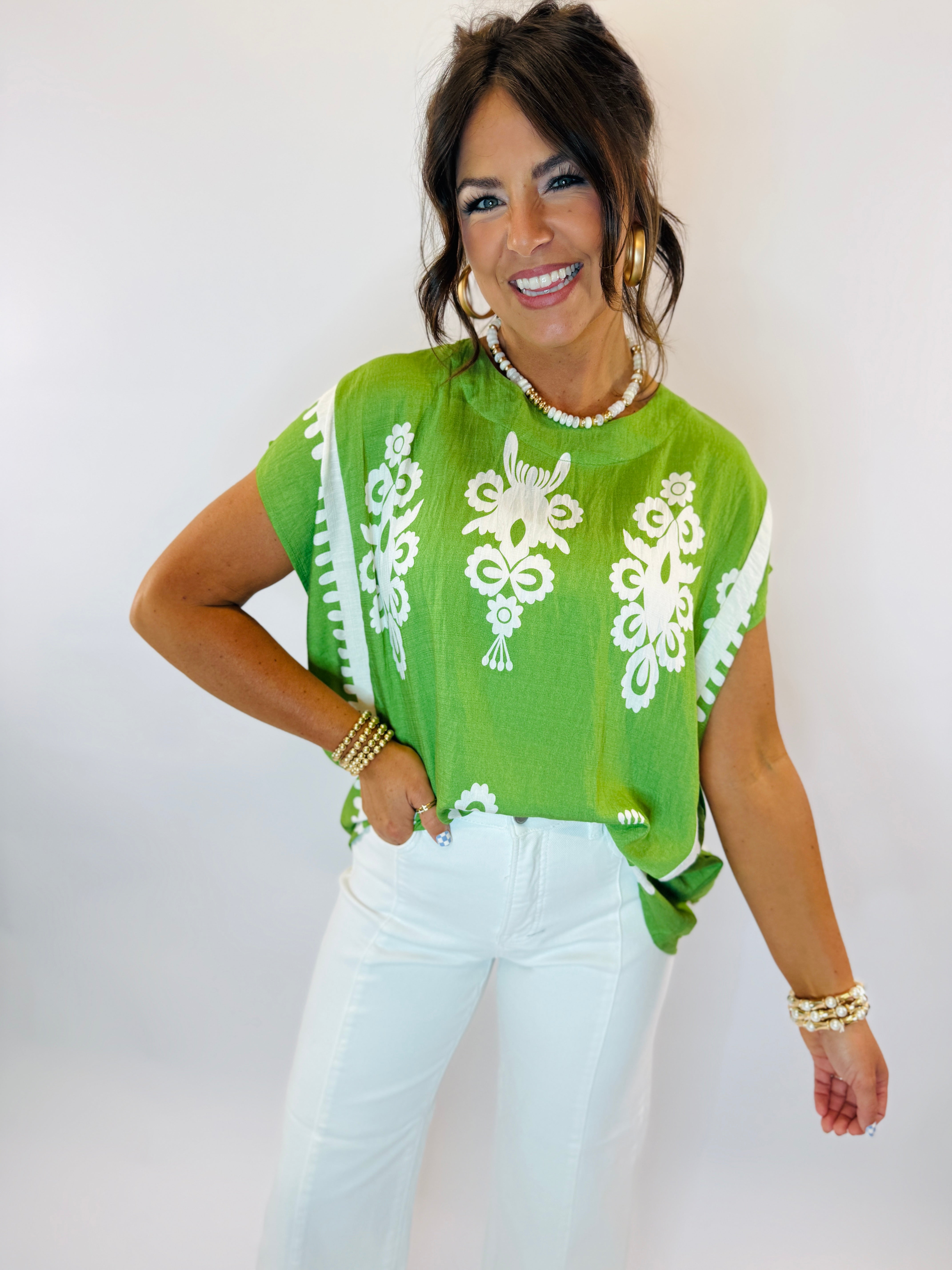 Woman wearing bright green Rylee top with white floral embroidery paired with white pants and pearl necklace.