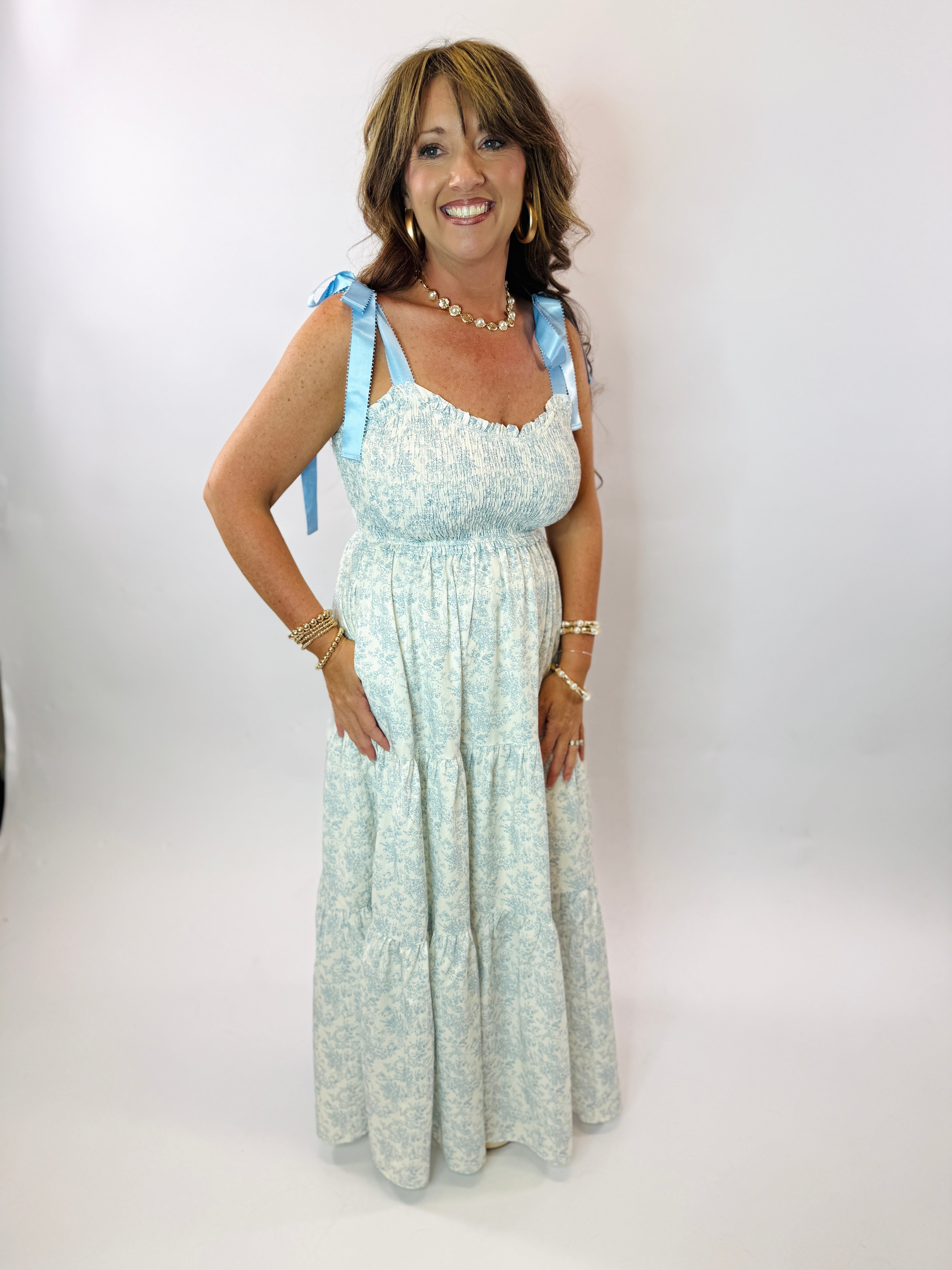 Woman wearing light blue floral maxi dress with tie shoulder straps and smocked bodice