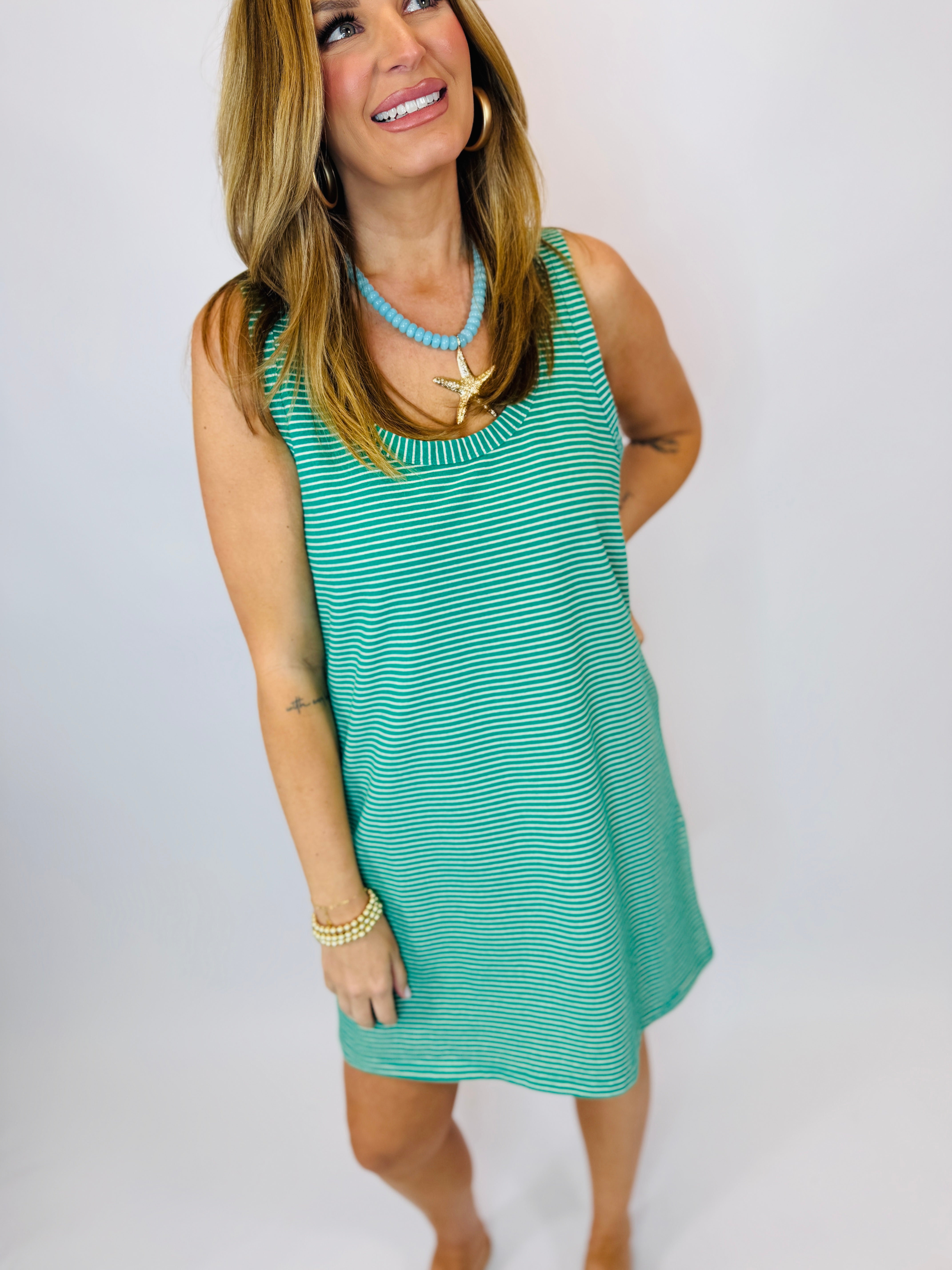 Woman wearing turquoise and white striped sleeveless mini dress with beaded necklace and gold jewelry accessories.