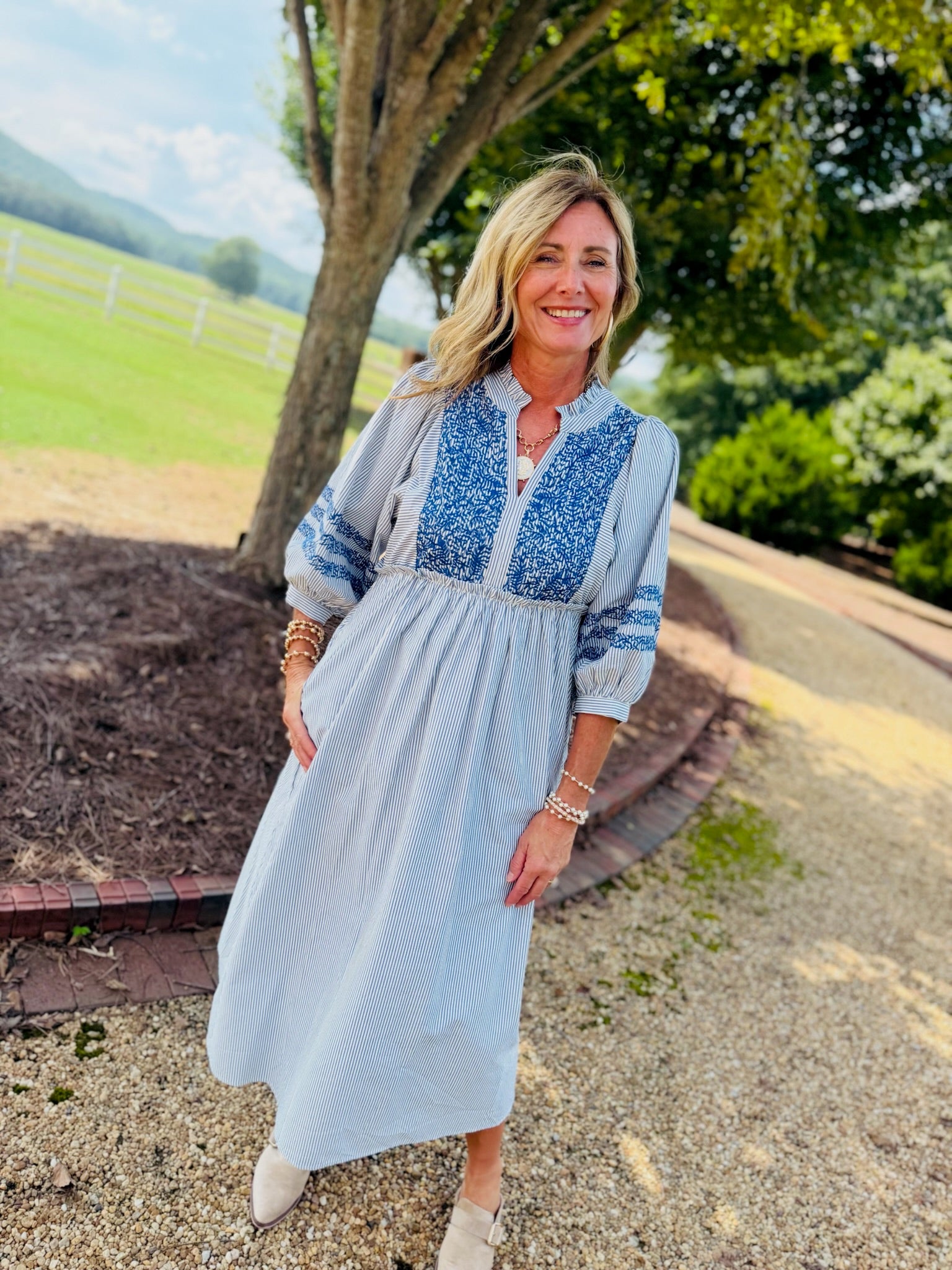 Woman wearing Sherri Dress in blue striped midi length with embroidered bodice and three-quarter sleeves.